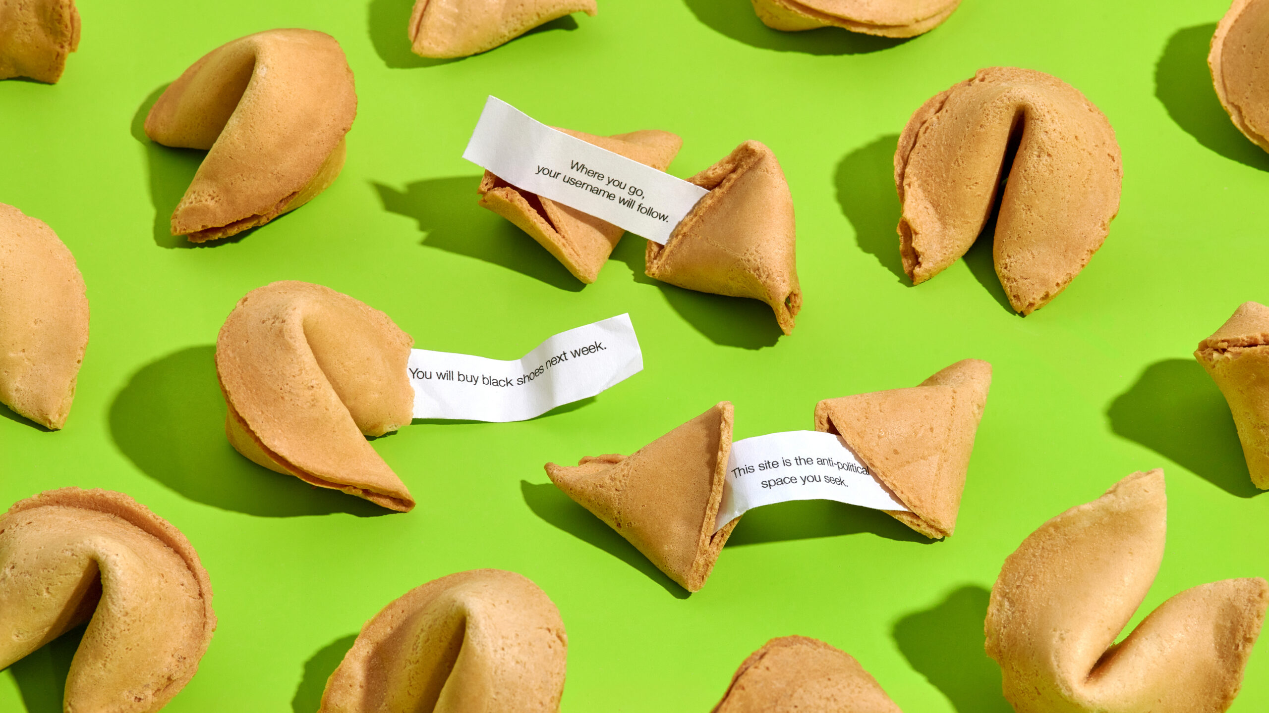 A number of fortune cookies on a green surface, three of which have exposed fortunes reading "Where you go, your username will follow," "You will buy black shoes next week," and "This site is the anti-political space you seek."