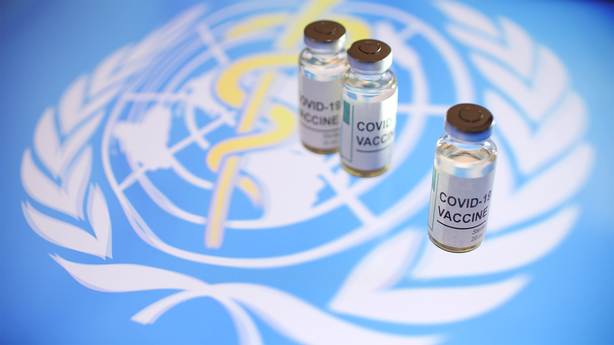 Three vials of COVID-19 vaccine in front of the World Health Organization's logo.