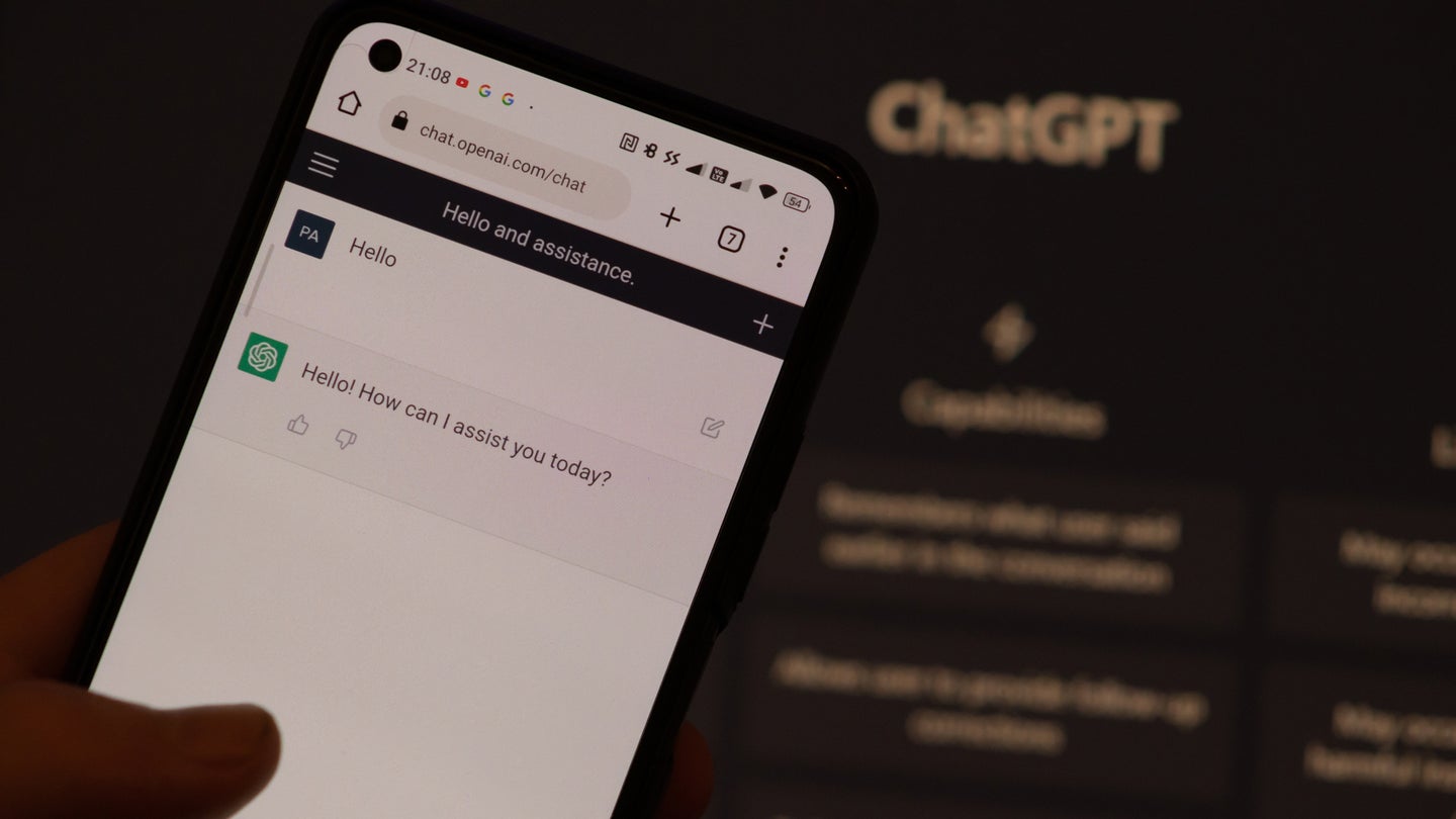 Phone showing ChatGPT chat screen against backdrop of website homepage