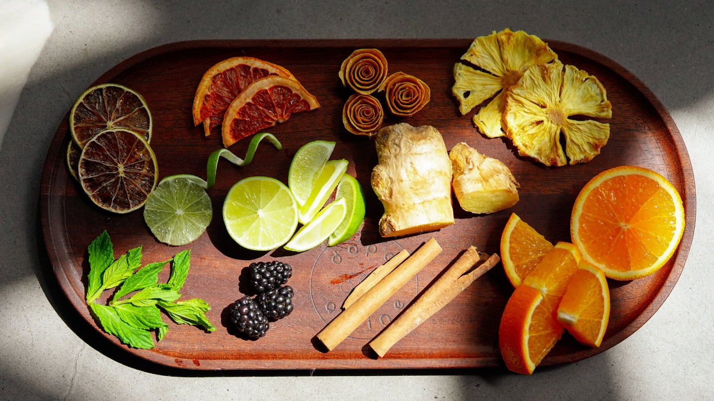 A wooden serving tray with a variety of dehydrated fruit and herbs on it, along with fresh fruit and herbs.