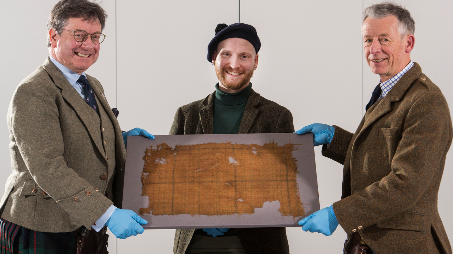 Scottish Tartans Authority chair John McLeish (right) and tartan historian Peter MacDonald (left), bring the Glen Affric tartan to V&A Dundee curator James Wylie (center) to be exhibited for the first time at the museum.
