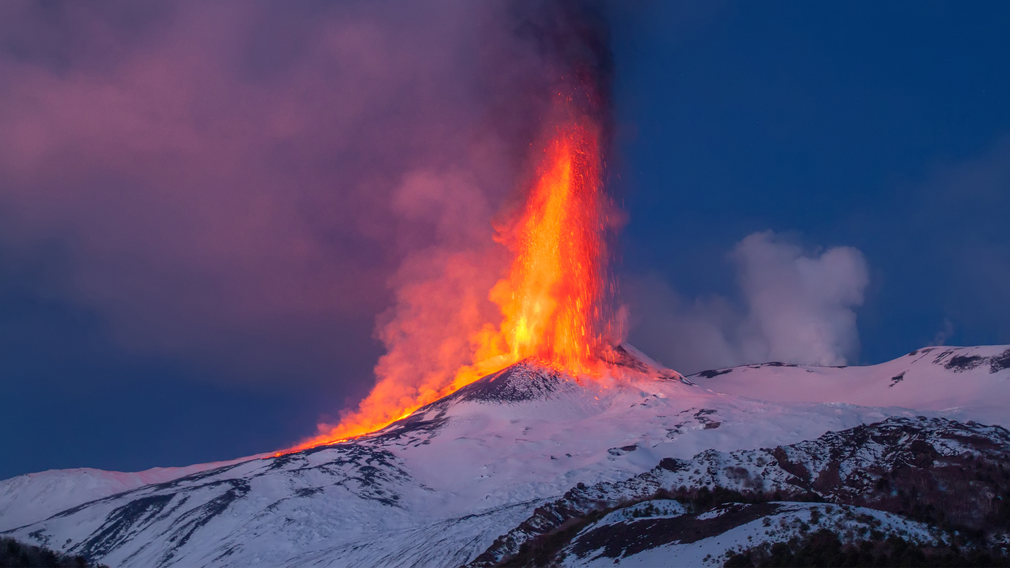 Mount Etna in Italy spews lava with snow around the top of the volcano.