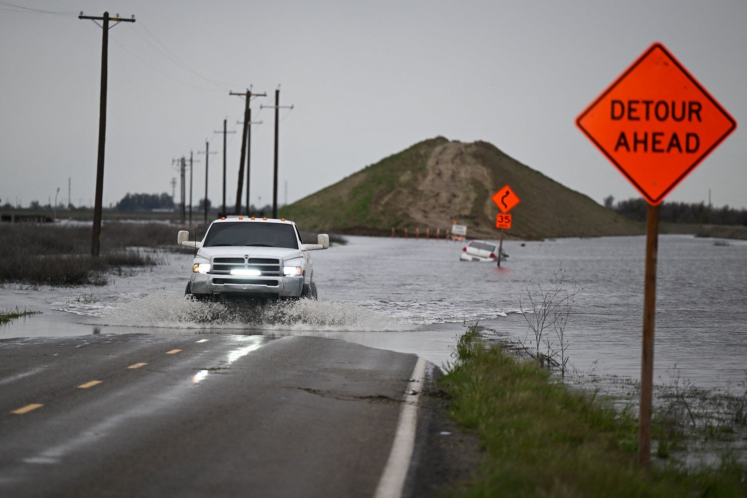 Pickup truck trying to cross flooded road marked by an orange detour sign in Tulare Lake Basin, California. 