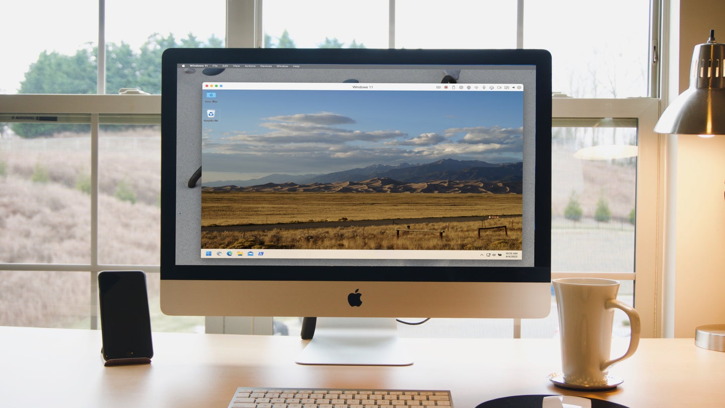 A desktop Mac computer running Windows 11 in a virtual machine. The computer is on a desk in front of a window that looks out onto a grassy field.