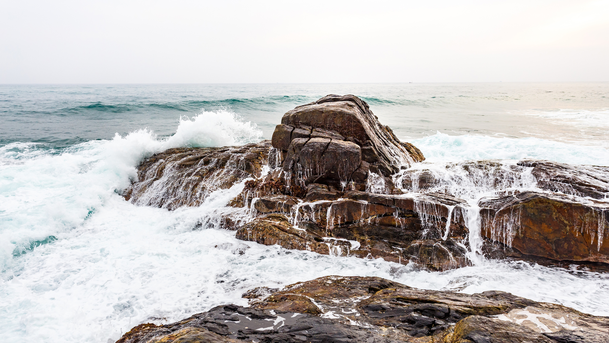 Ocean waves crashing on rocky shoreline on cloudy day.
