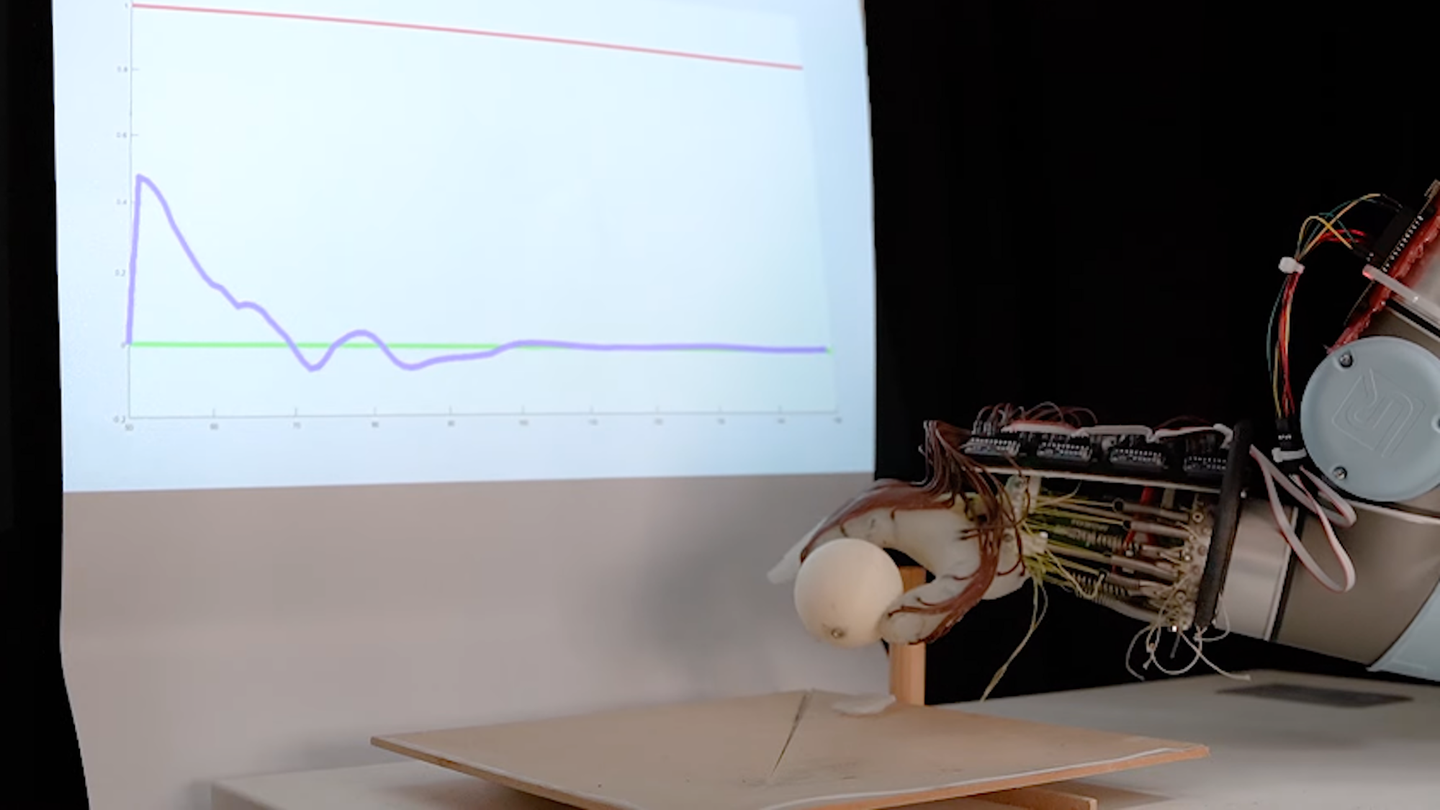 Soft robotic hand picking up plastic ball from table