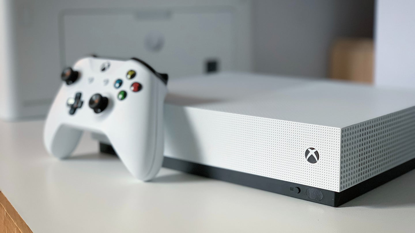 An Xbox One S with a controller sitting on a white table.