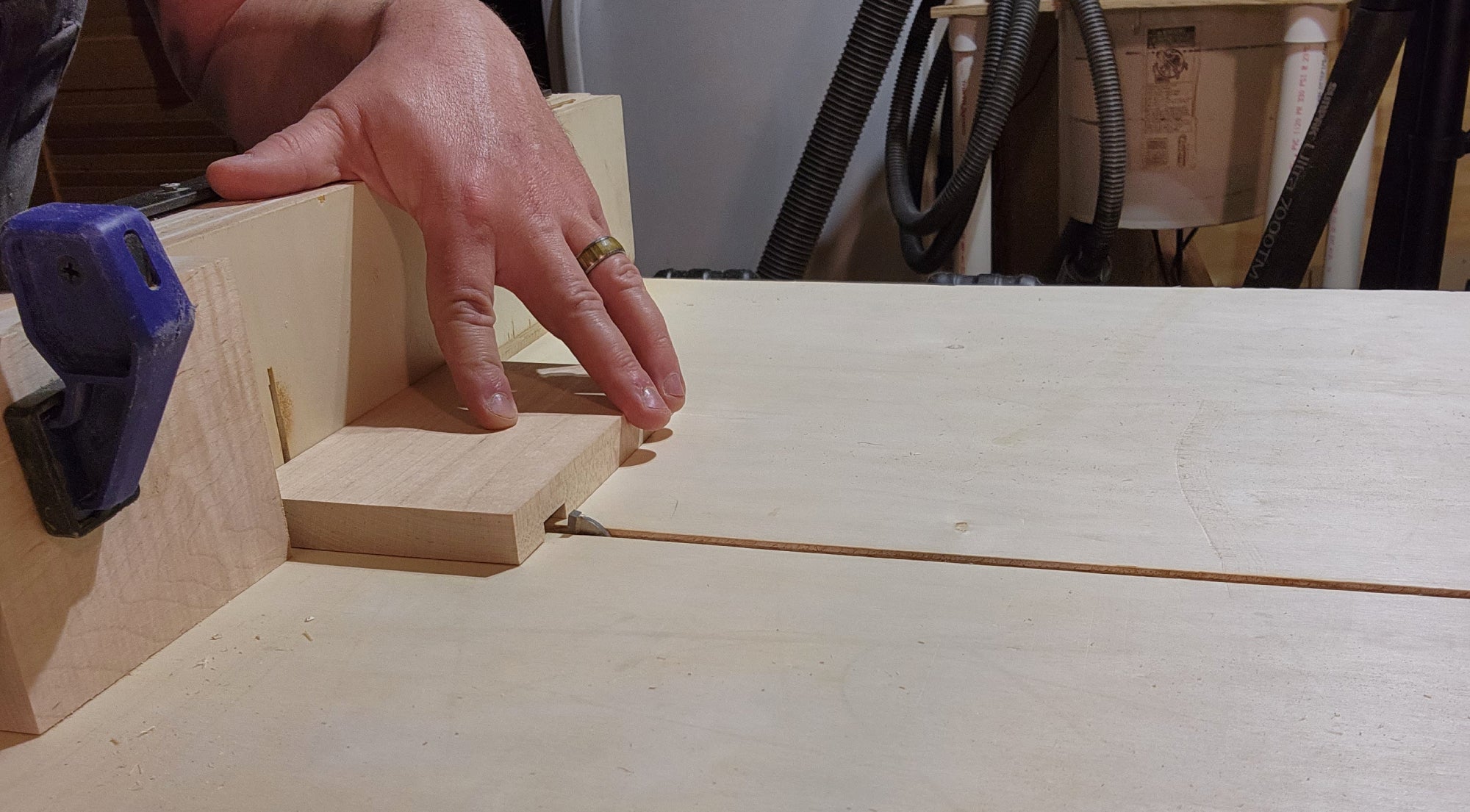 A man cutting a dado in a wooden egg holder leg piece using a crosscut sled on a table saw.