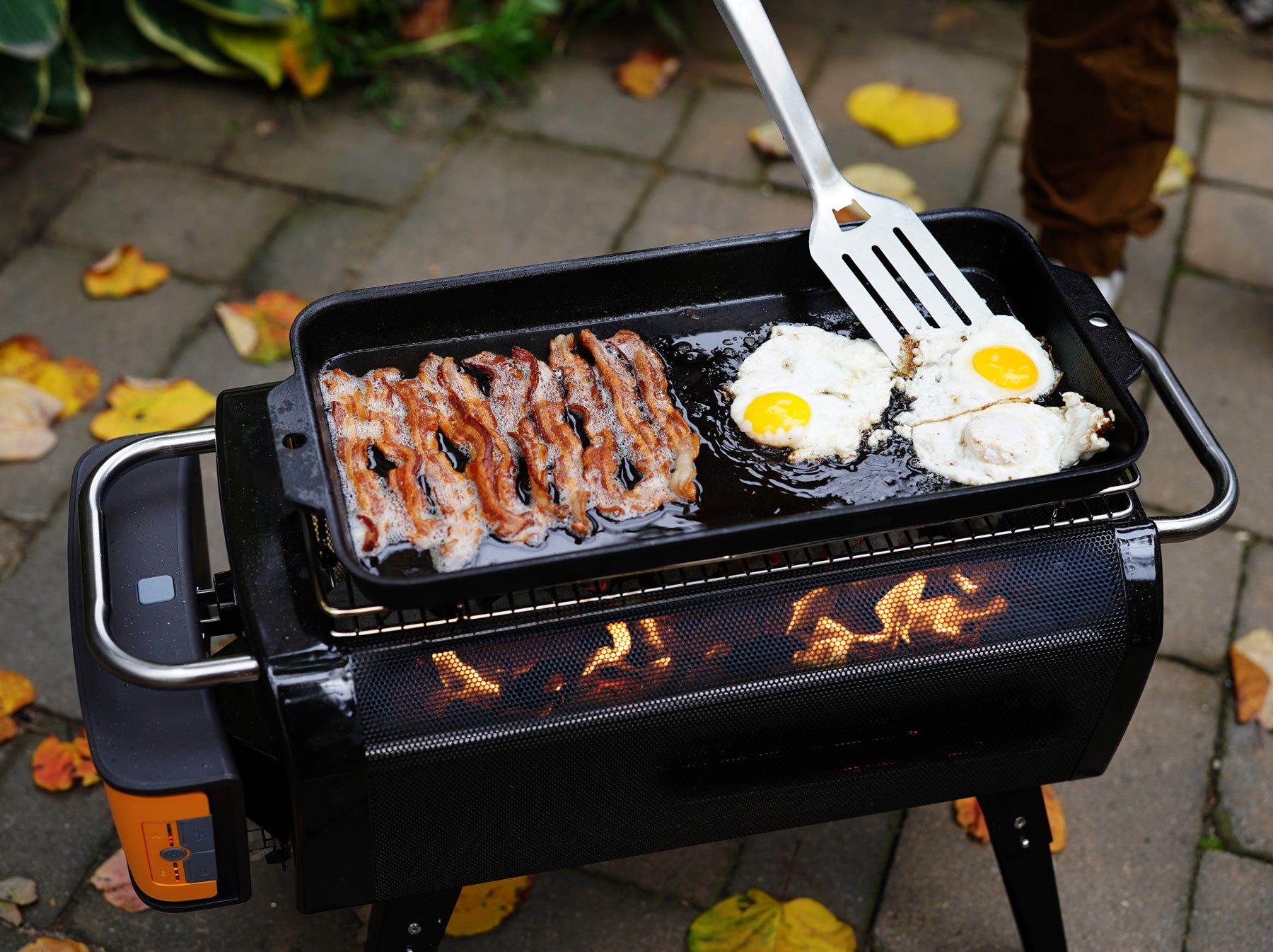Biolite FirePit+ with the included grill grate and a pan cooking eggs and bacon