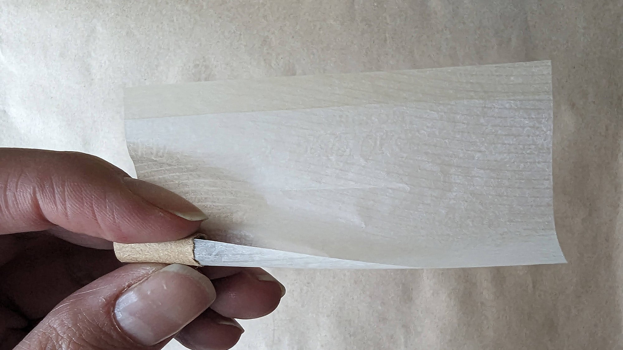Hand holding a smoking paper with a cardboard tip on the left side.