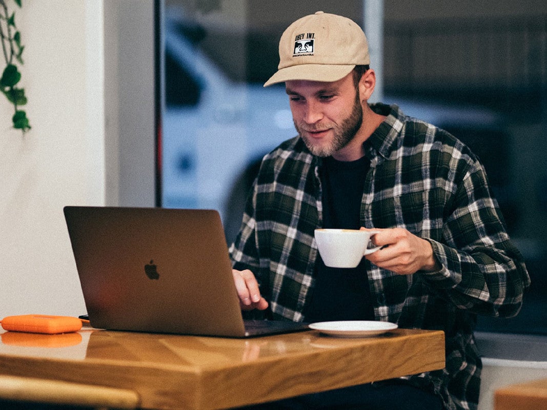 A person sitting at a laptop and drinking a cup of coffee.