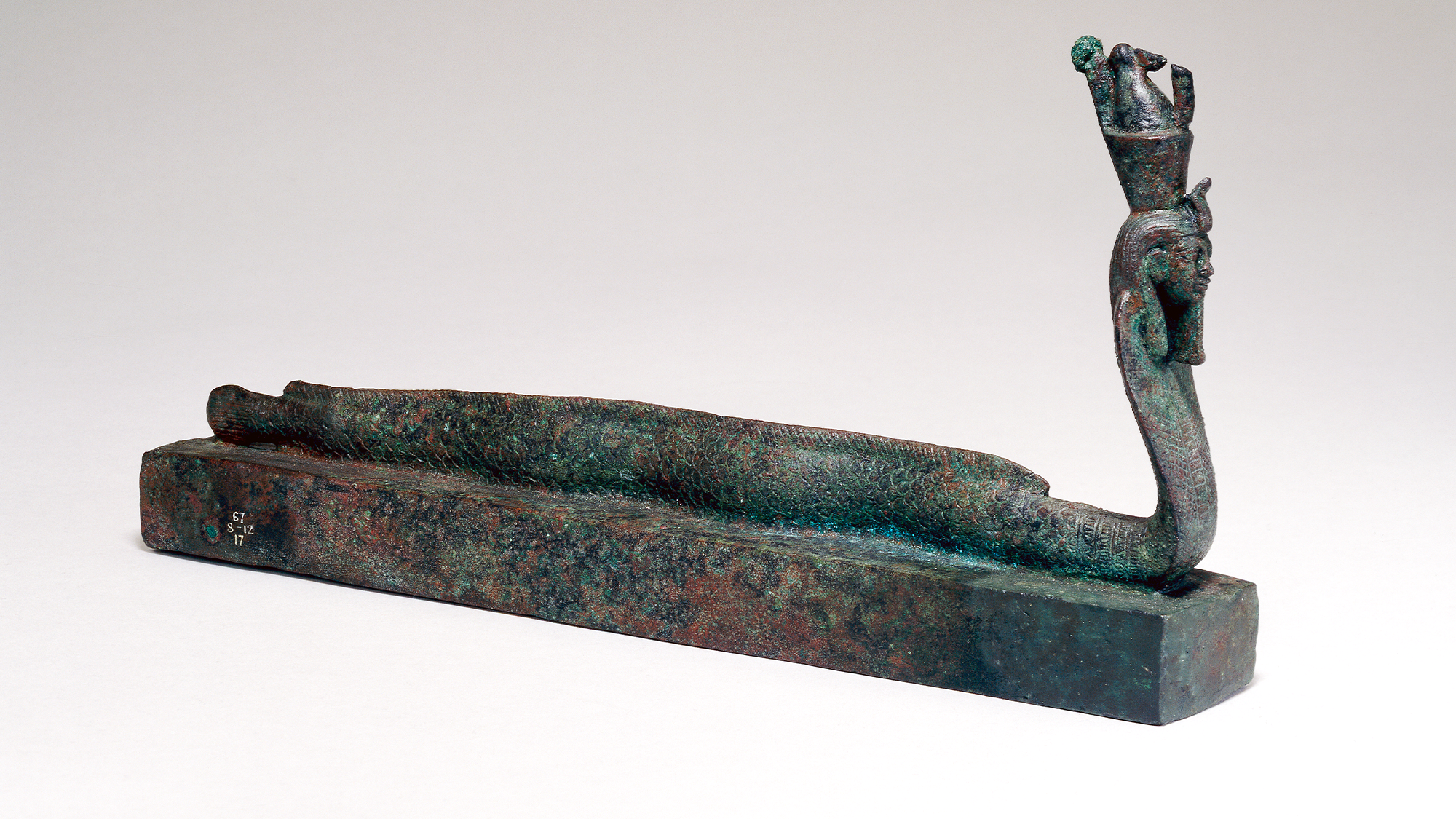 An animal coffin with a human-headed part-eel, part-cobra figure wearing a double crown. The figure is associated with Atum, an ancient Egyptian god of pre-existence and post-existence.