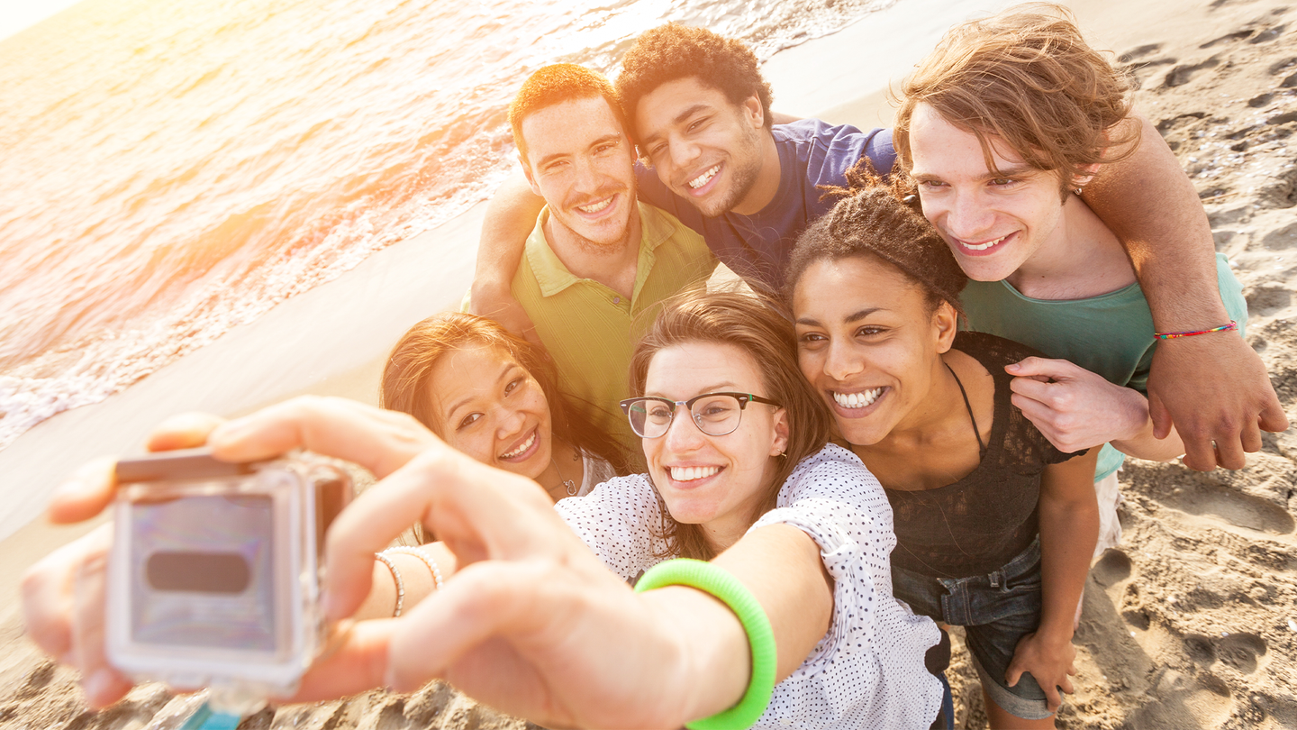 A group of six young people take a selfie on a beach.