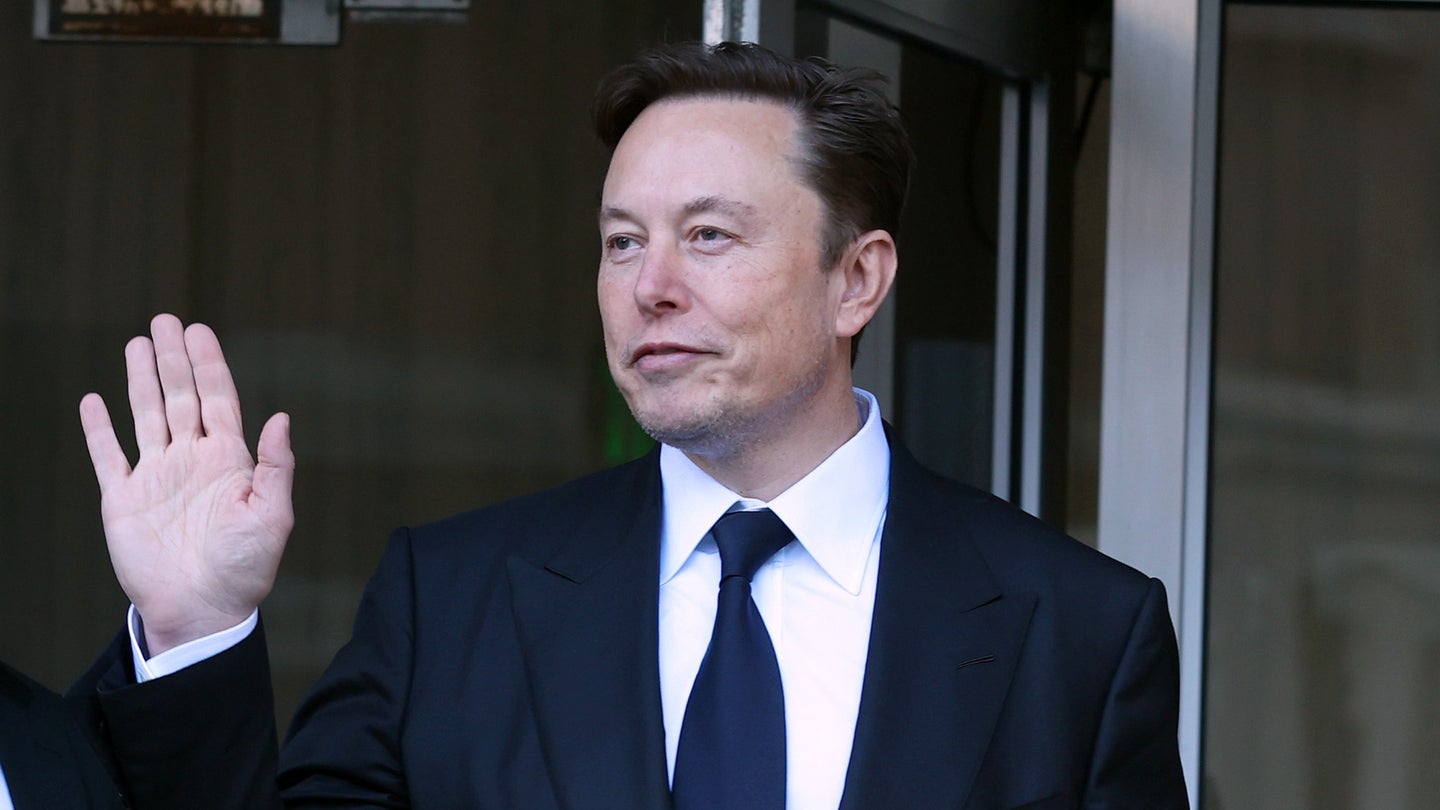 Elon Musk waving while wearing a suit