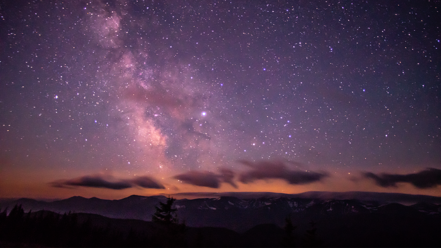 The Milky Way rises in a night sky with a pink hue.