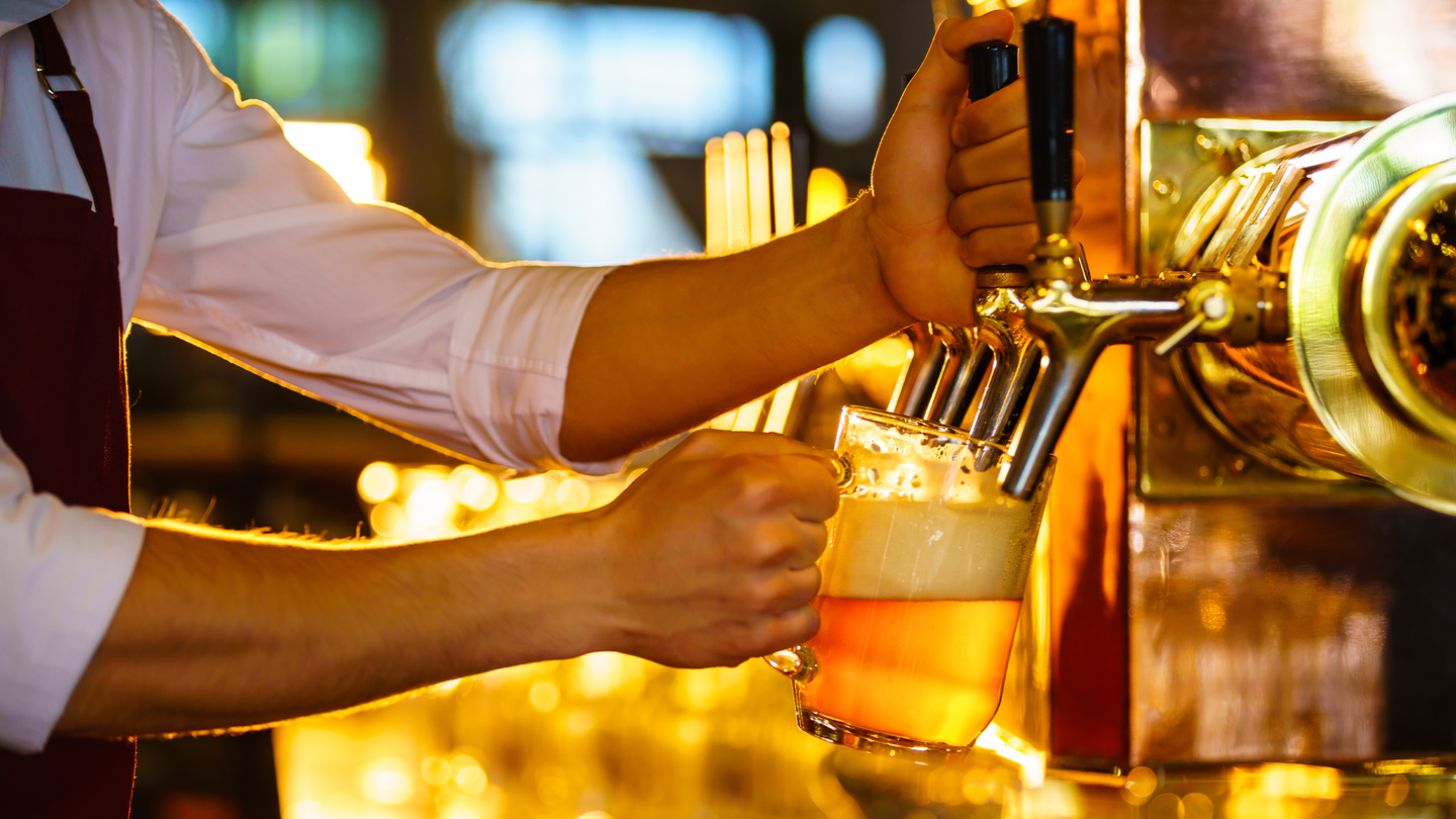 A bartender pours a light beer into a large glass.