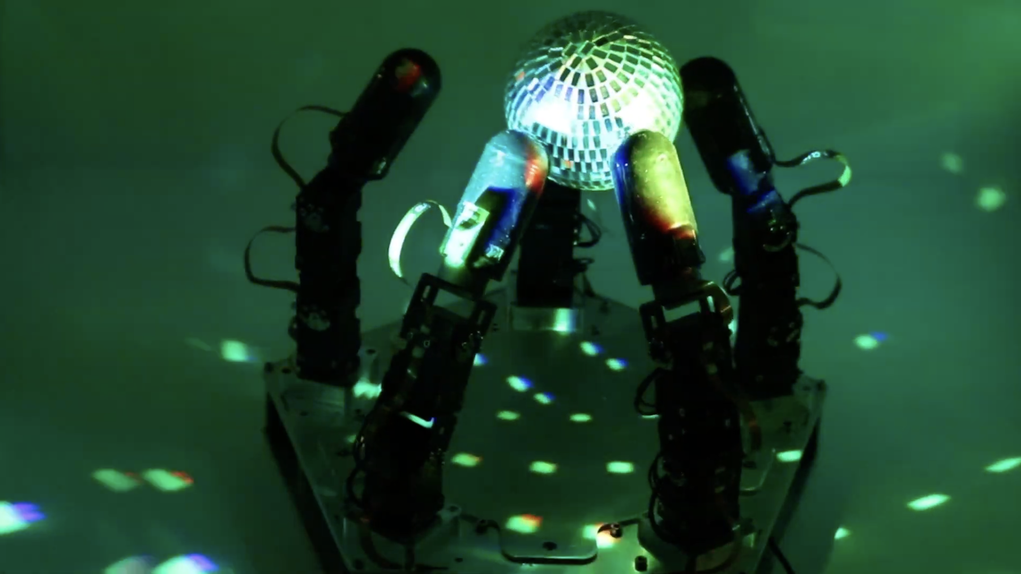 A robotic hand manipulates a reflective disco ball in dim lighting.