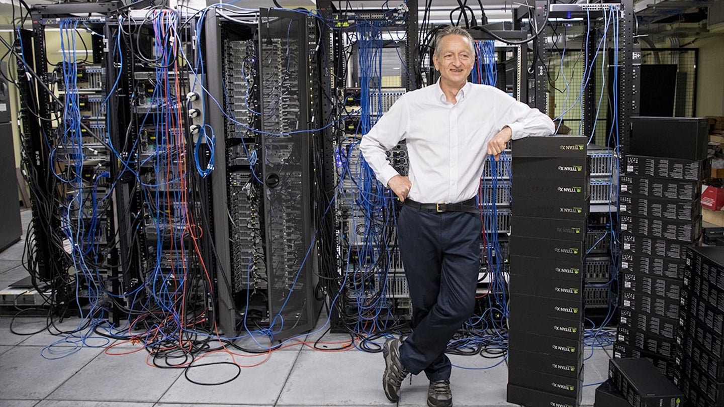 Geoffrey Hinton stands in front of array of computer systems