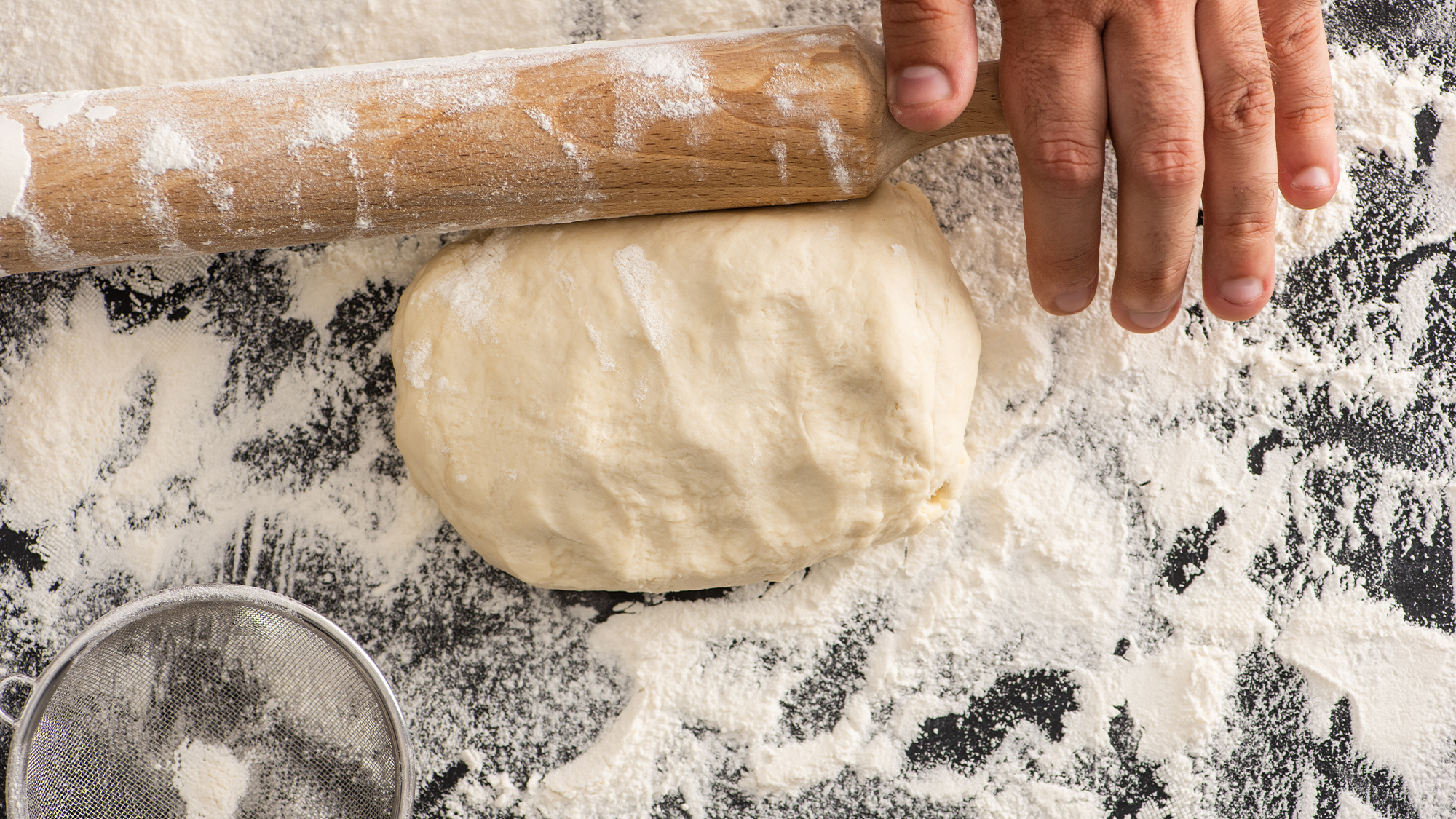 Dough being rolled out with flour sprinkled around it.