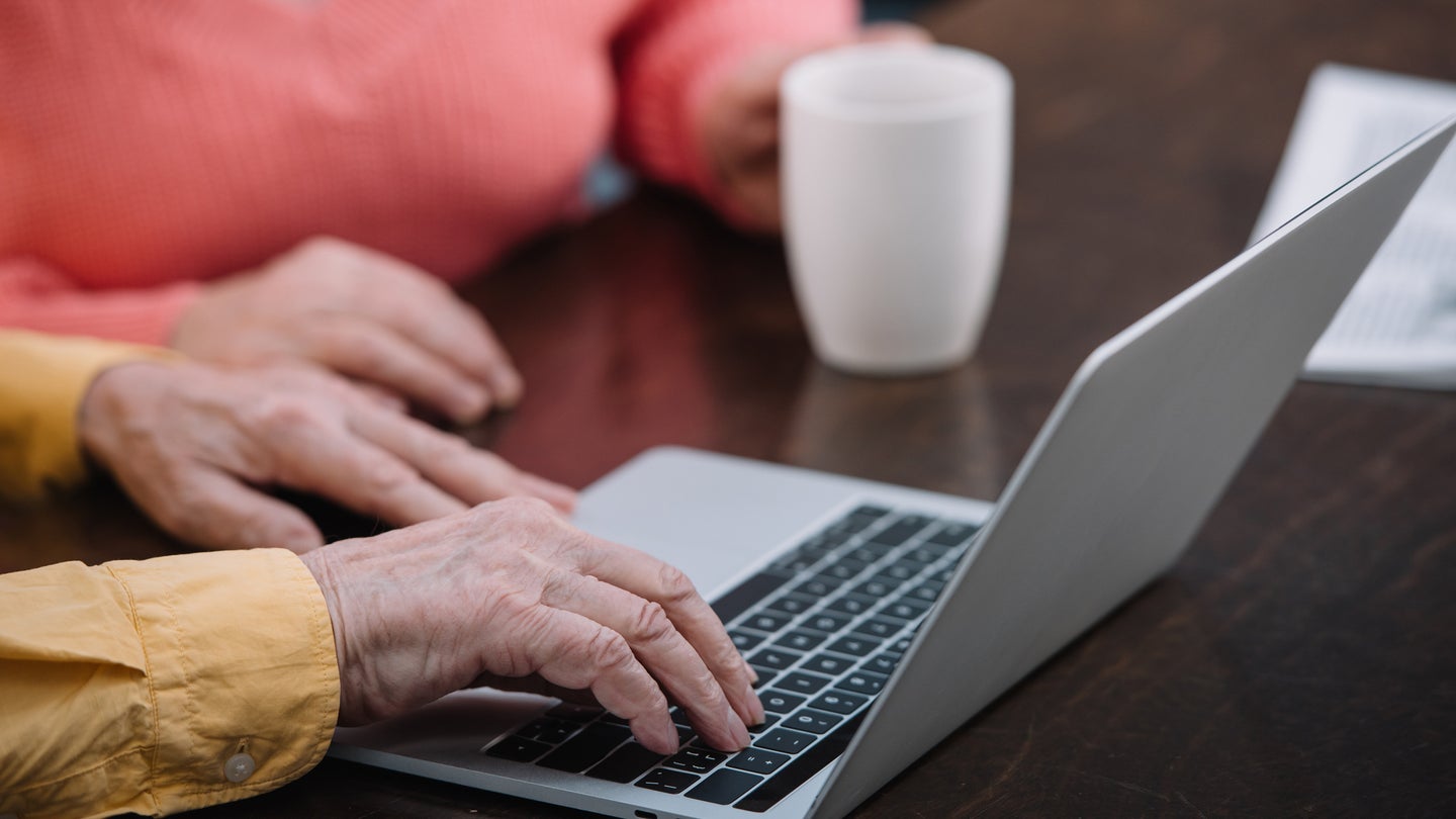 Senior citizen hands typing on laptop keyboard