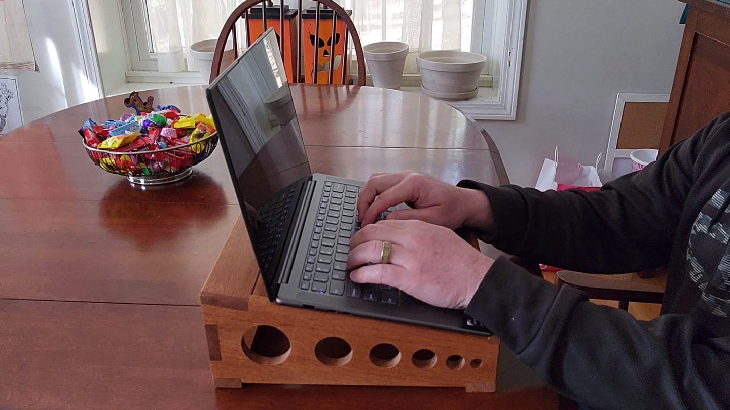 A man wearing a black sweatshirt using a laptop on a DIY wooden laptop stand on a wooden table.