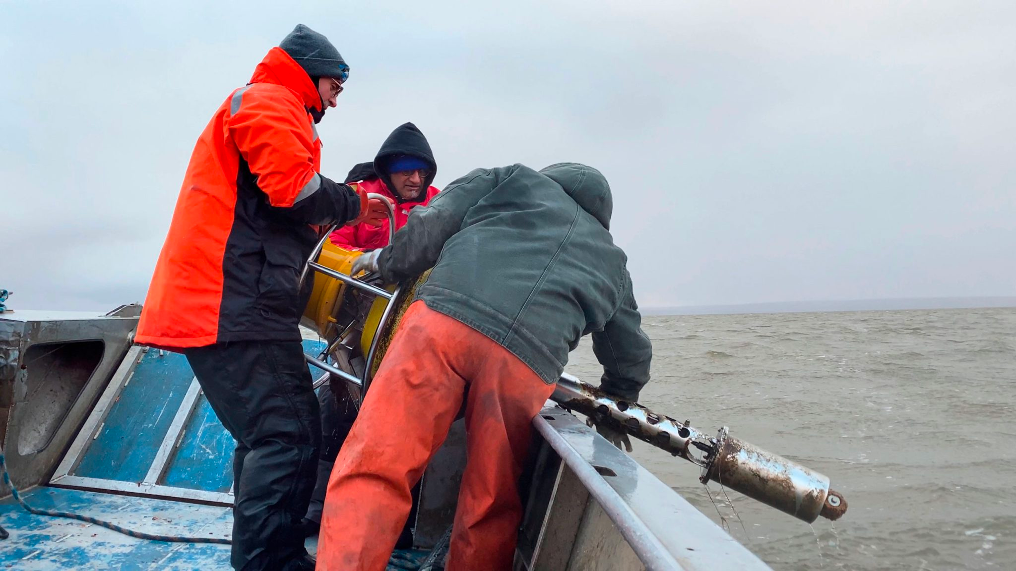 Environmental scientists in waterproof gear drop water-monitoring equipment into the waters off Kotzebue, Alaska