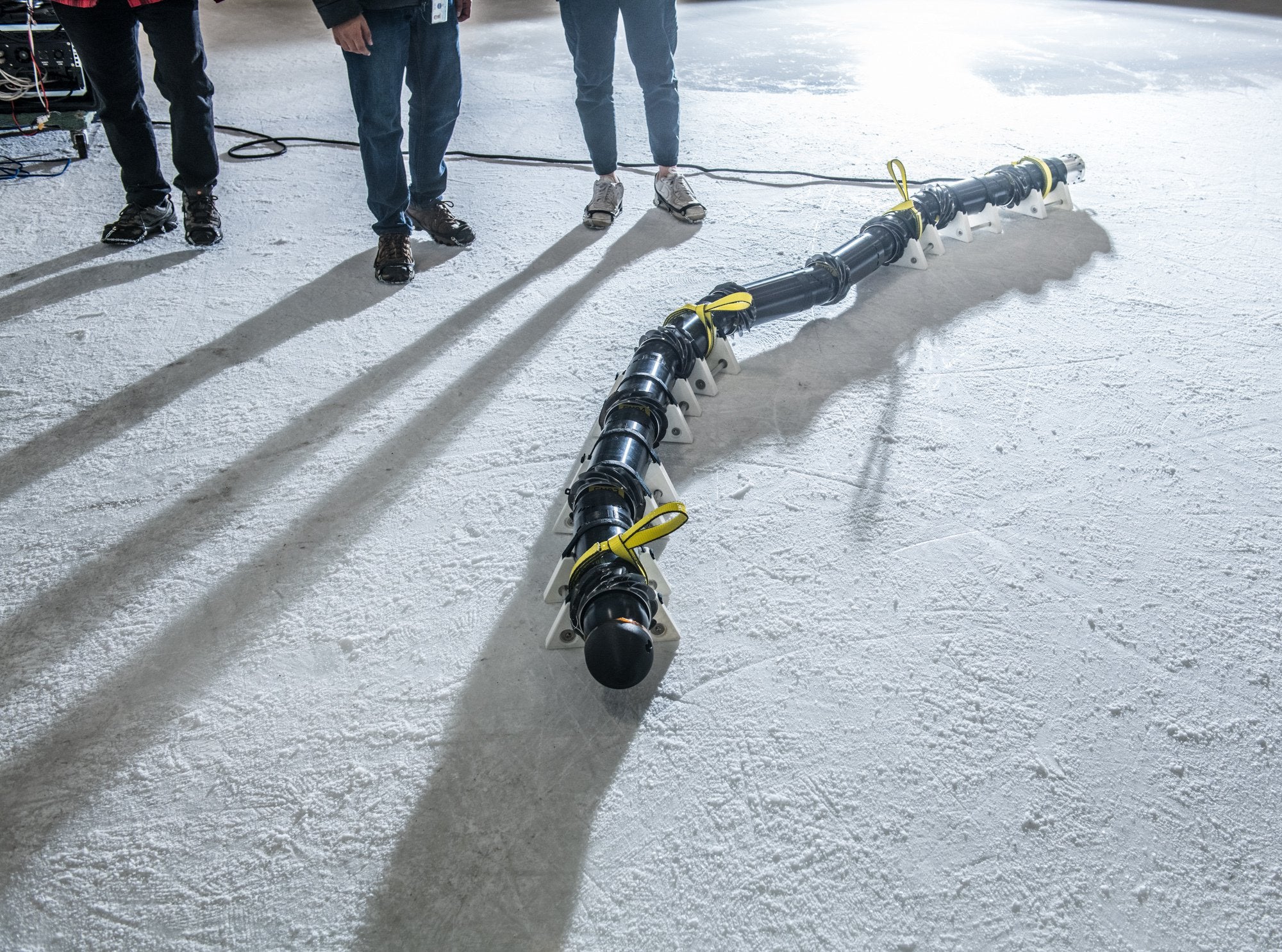 NASA EELS snake robot in ice skating rink next to researchers.