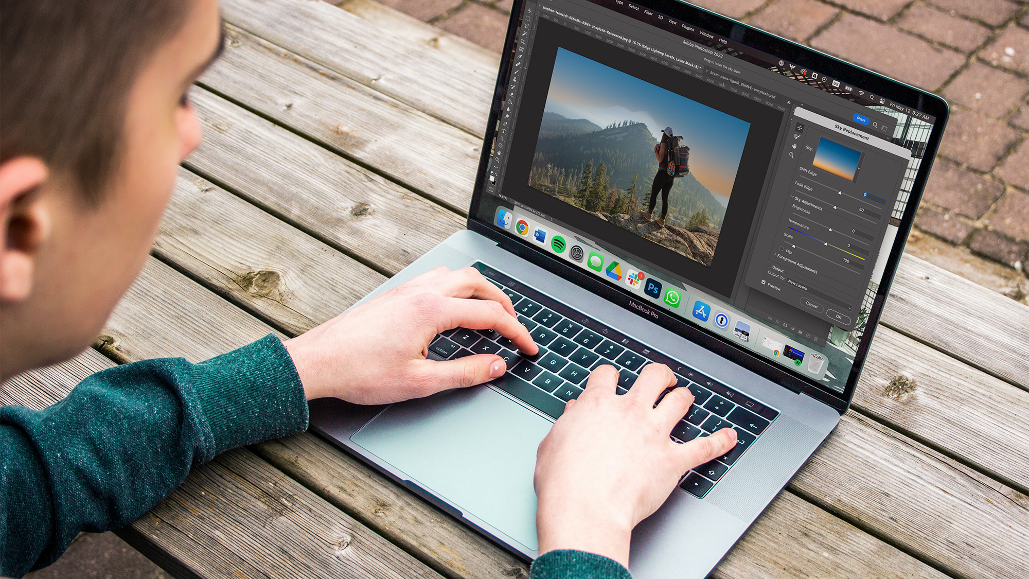 A person typing on a laptop and editing on photoshop.
