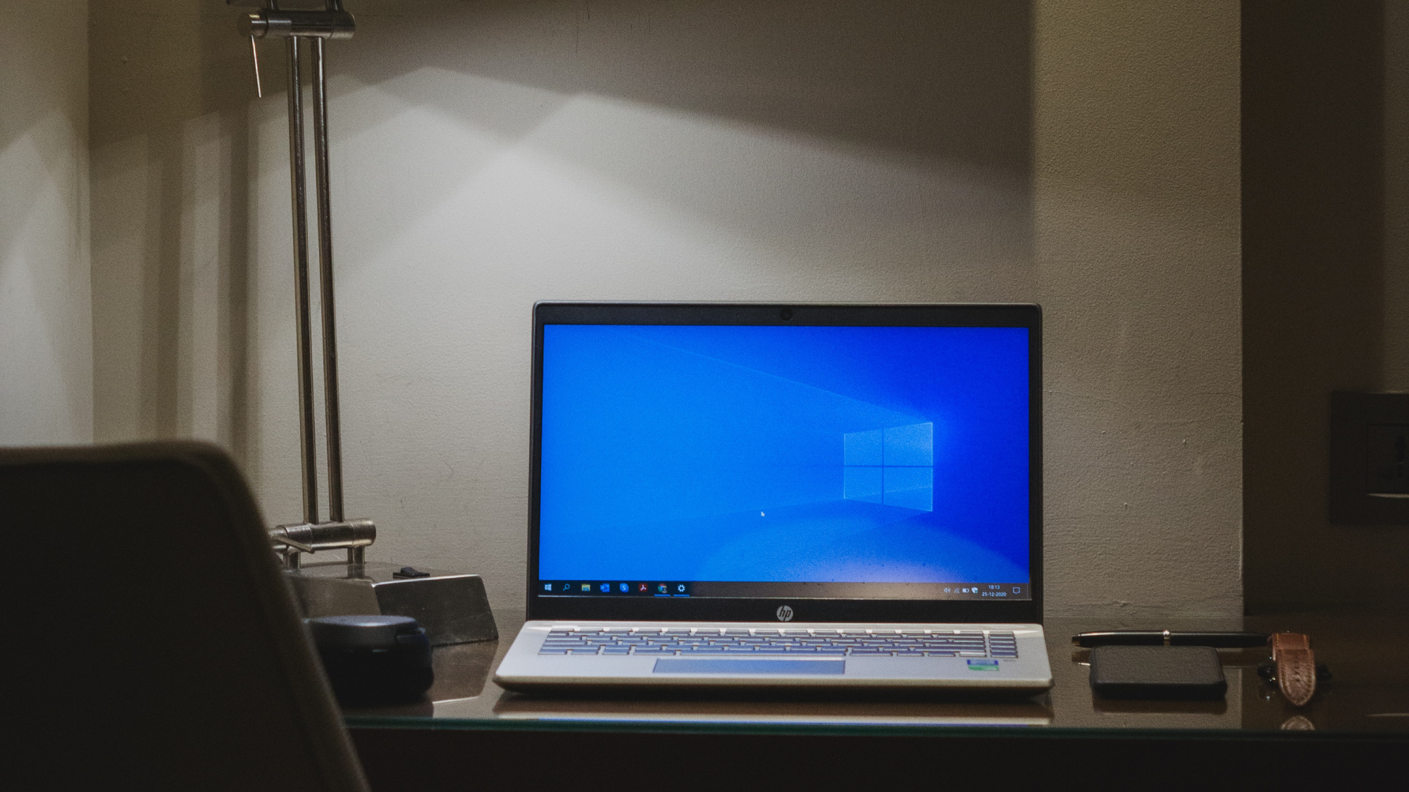 A Windows 10 laptop on a desk under a desk lamp, with the Windows desktop on the screen.