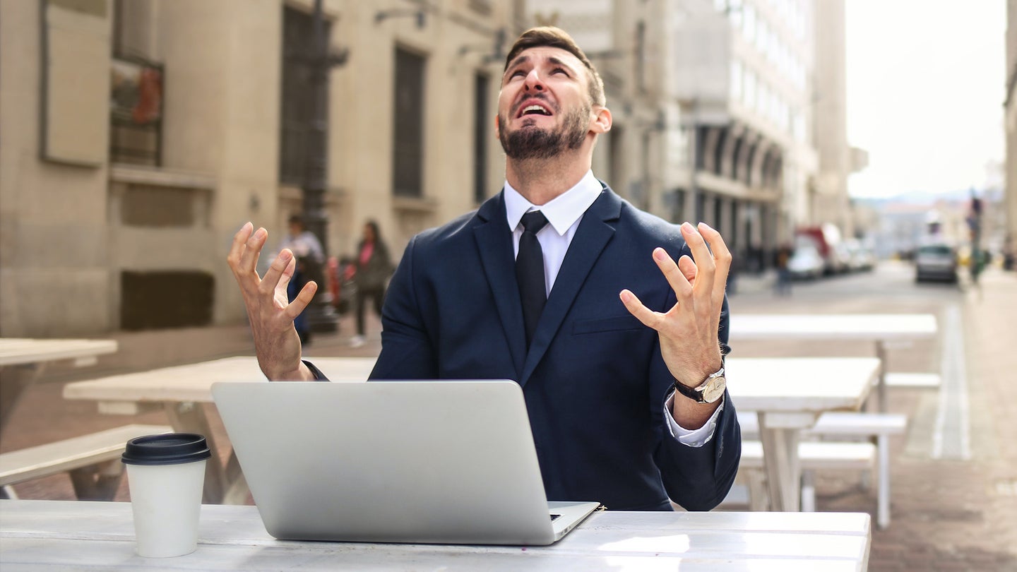 Person in a suit and tie sitting outside in front of their computer, looking frustrated.
