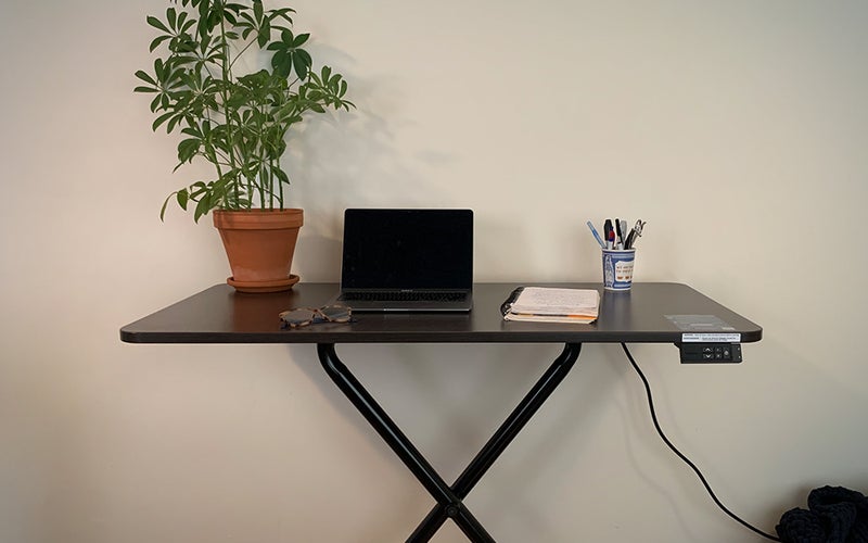 A Lillipad standing desk adorned with a laptop, plant, notebook, and pen holder