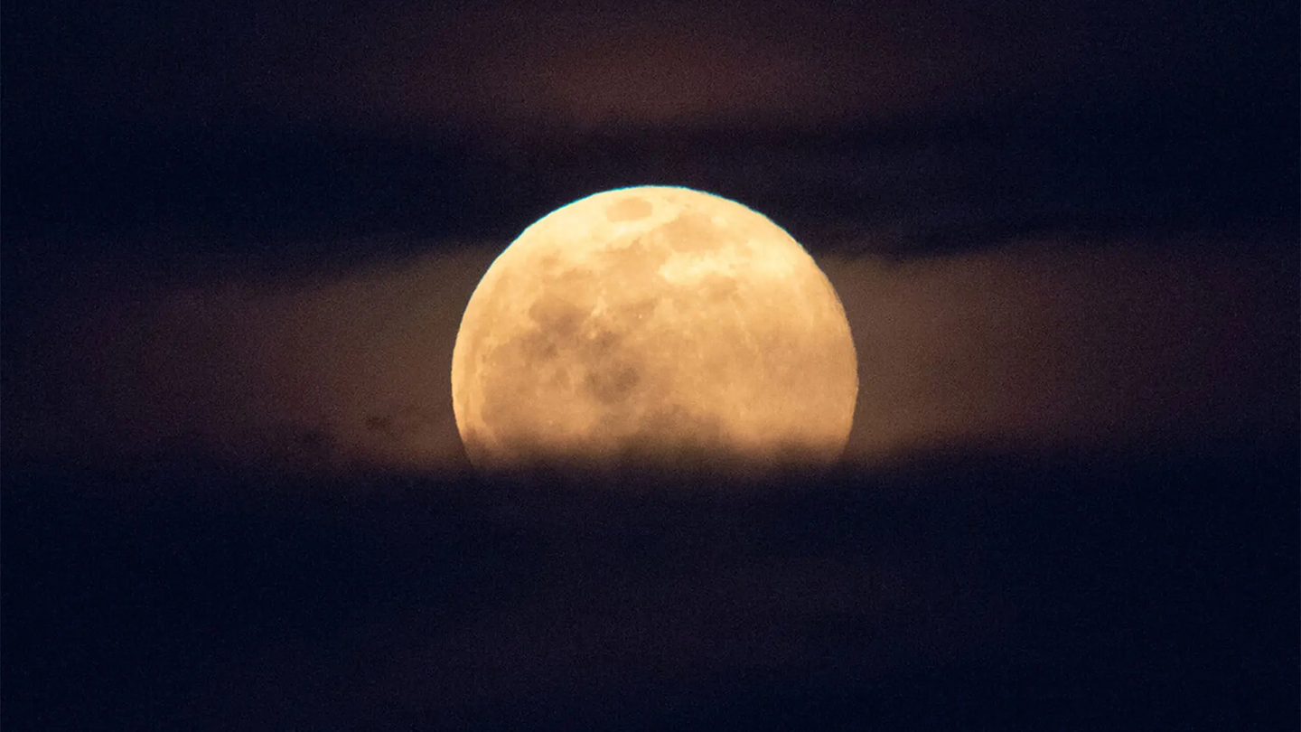A full moon rises with clouds below. June's Strawberry Moon peaks on June 3.
