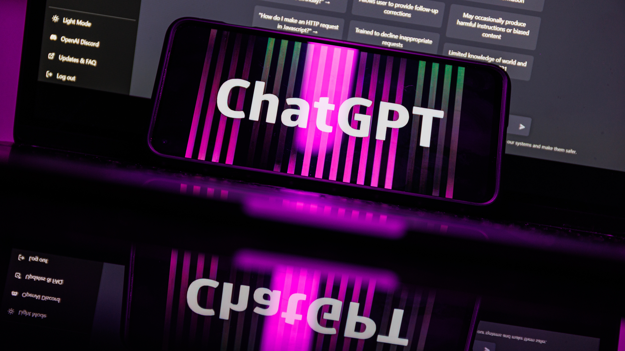 Smartphone showing ChatGPT logo resting on laptop with ChatGPT home page displayed