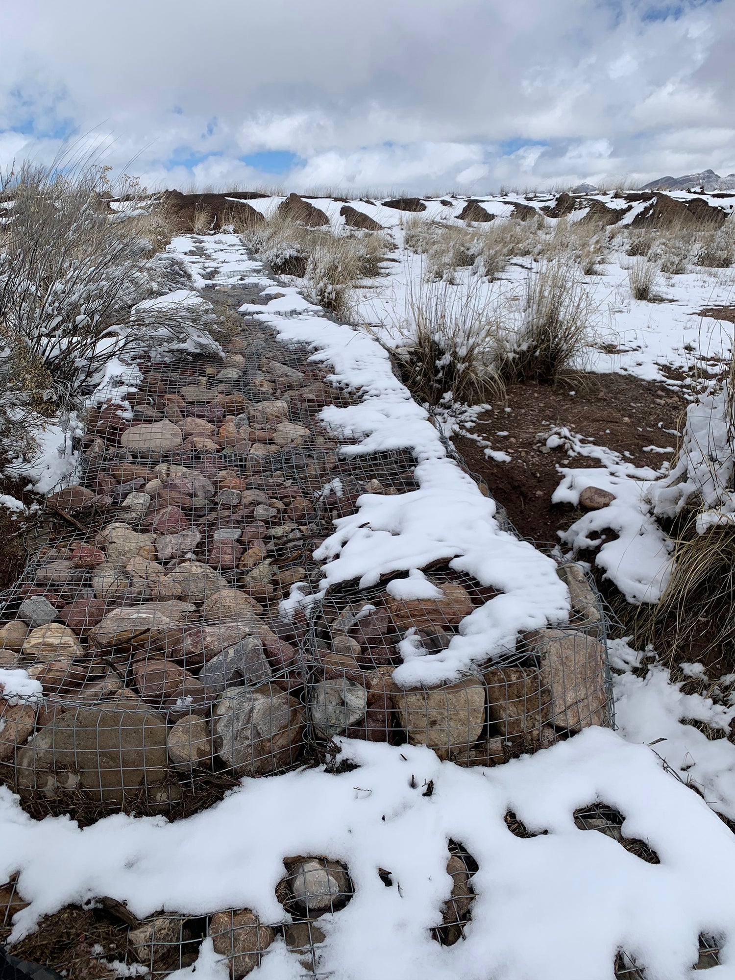 Pile of rocks captured in wire fencing with snow on top. Called gabions, they are built to slow water.