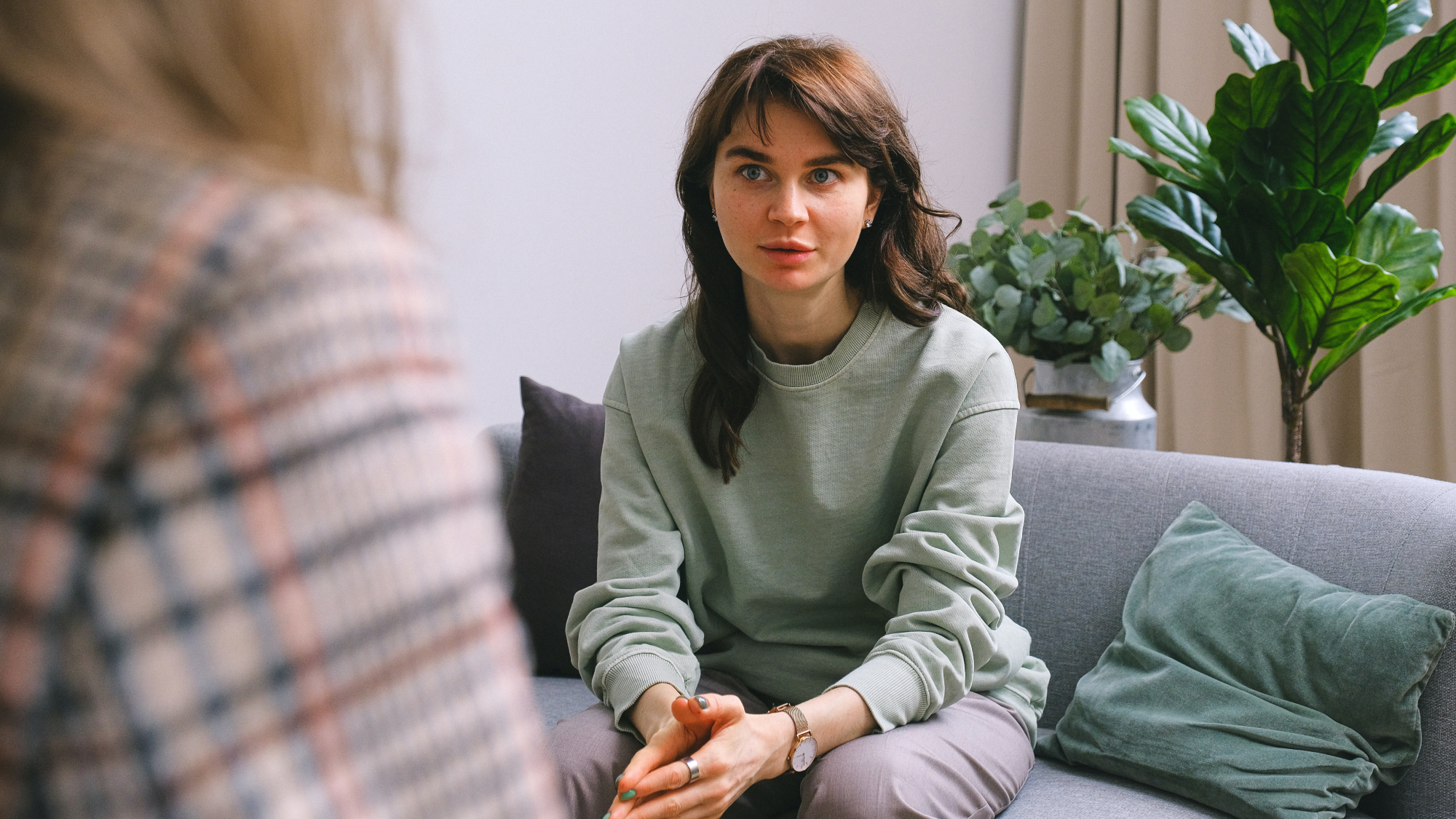 A concerned-looking person sitting on a couch with the back of another person in the foreground, perhaps a therapist talking with someone who has high rejection sensitivity.