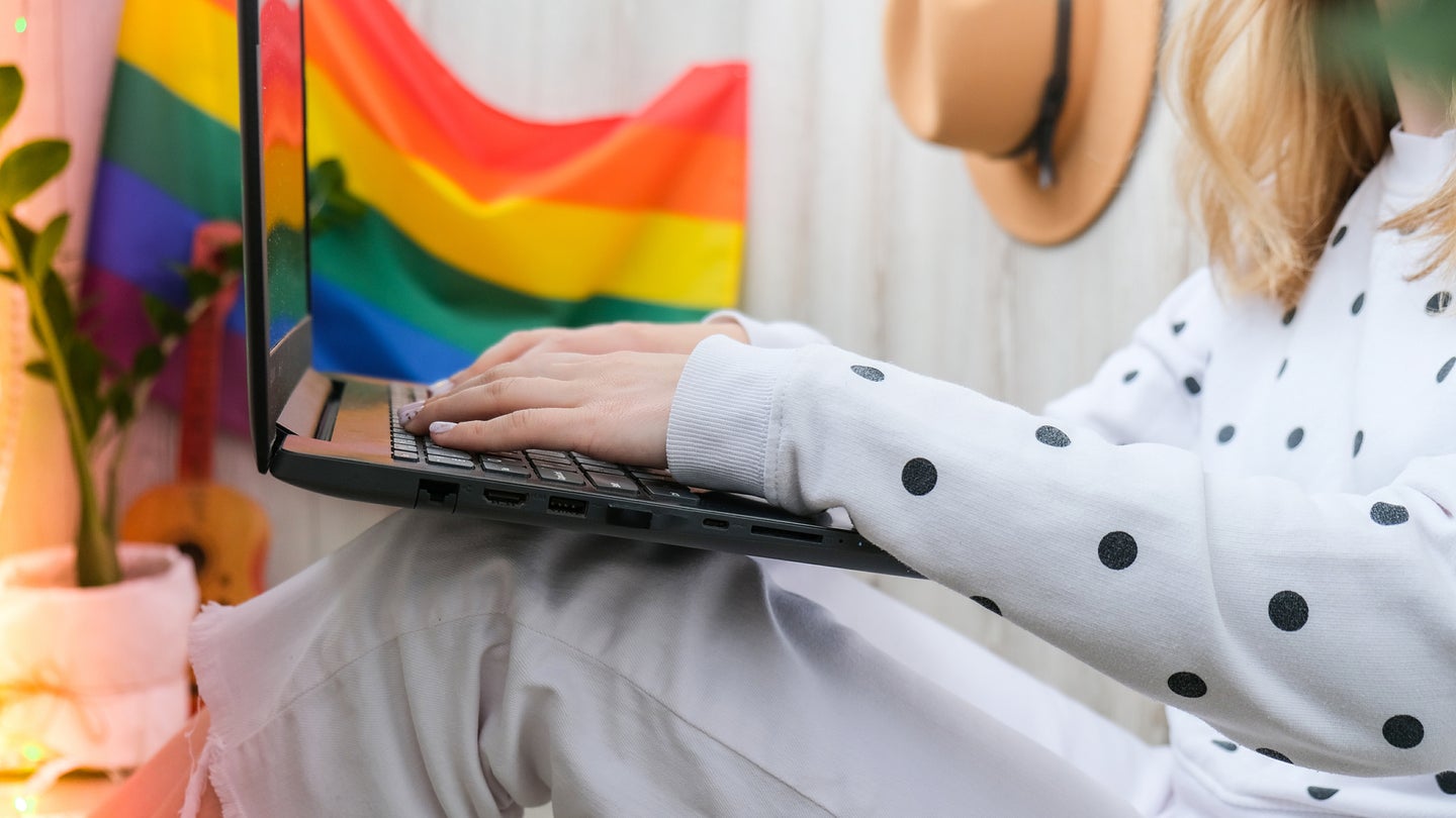 Woman using laptop with pride flag behind her