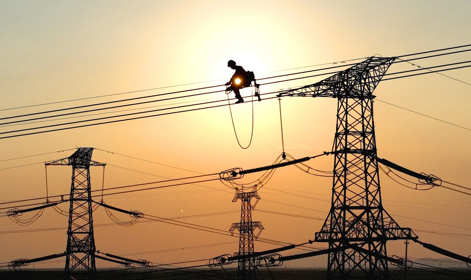An electrical worker suspended on high-voltage power lines in China against the sunset