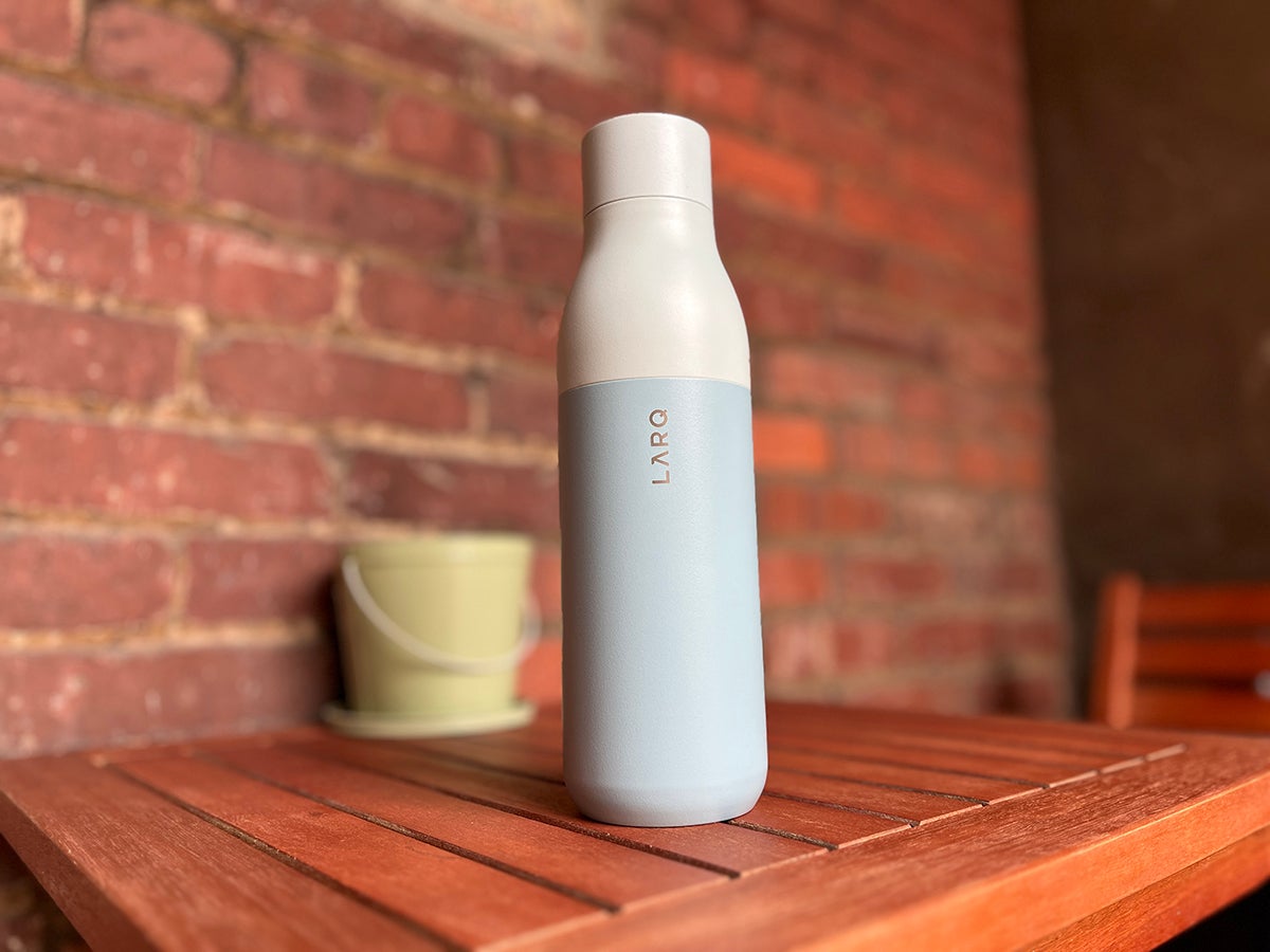A mint-colored insulated LARQ smart water bottle on a small wooden table in front of a brick background