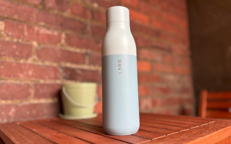 A mint-colored insulated LARQ smart water bottle on a small wooden table in front of a brick background