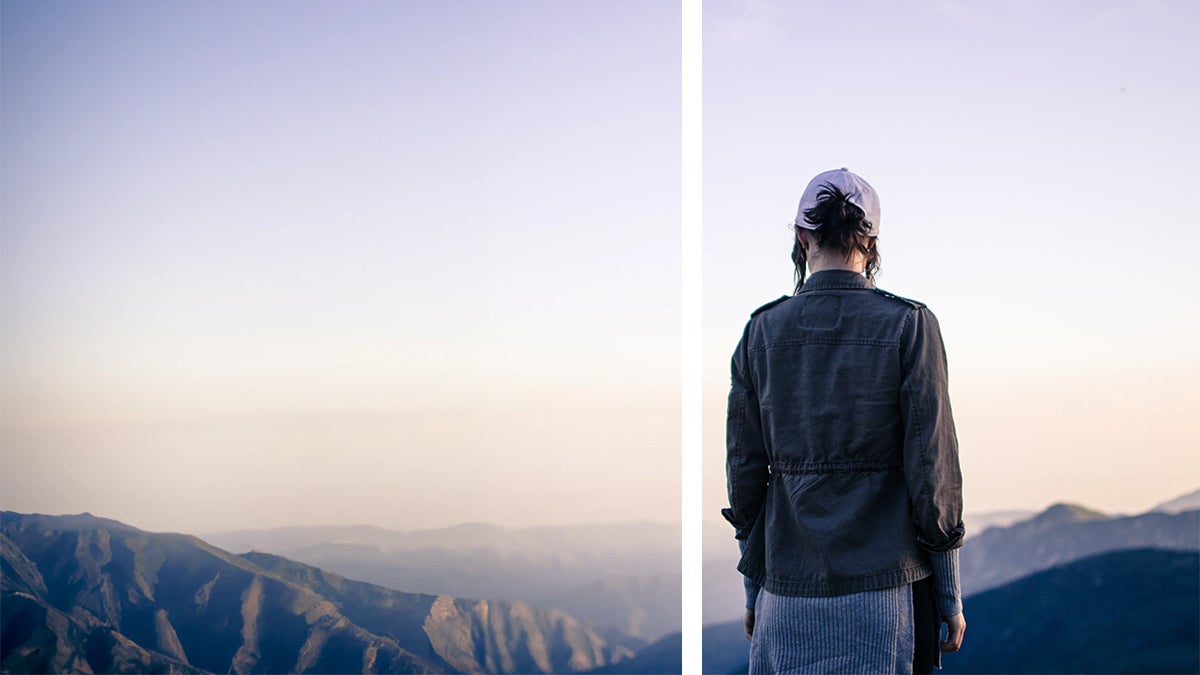 Человек в серой куртке и розовой бейсболке стоит на хребте и смотрит на горы на восходе солнца, а новые горы добавлены слева с помощью инструмента Dall-E 2 для расширения изображения AI.