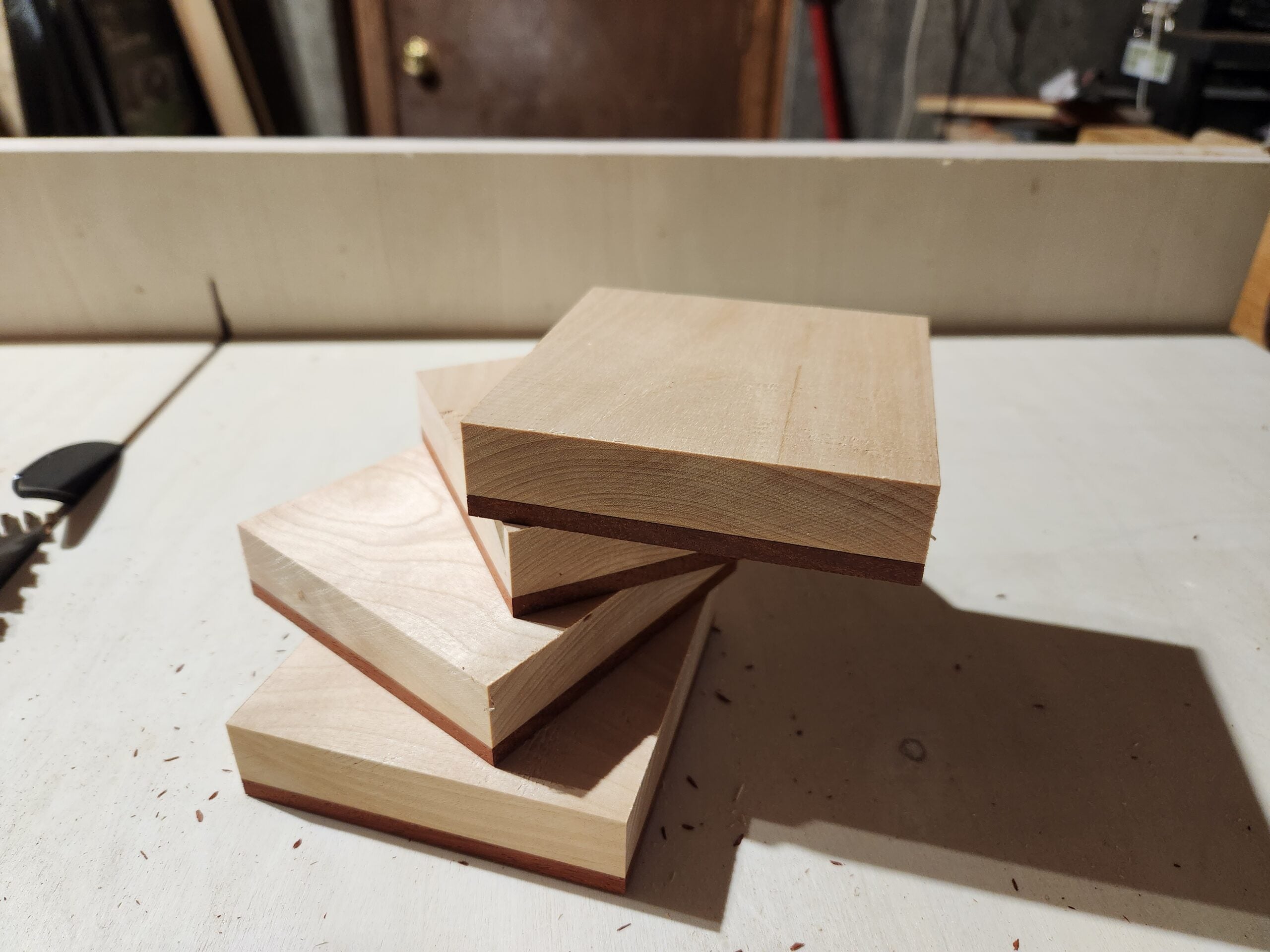 A stack of four pieces of laminated wood made out of one layer of maple and a thinner layer of padauk, on a table saw table.