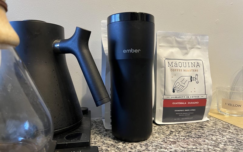 A black Ember smart mug on a marble countertop next to a bag of coffee