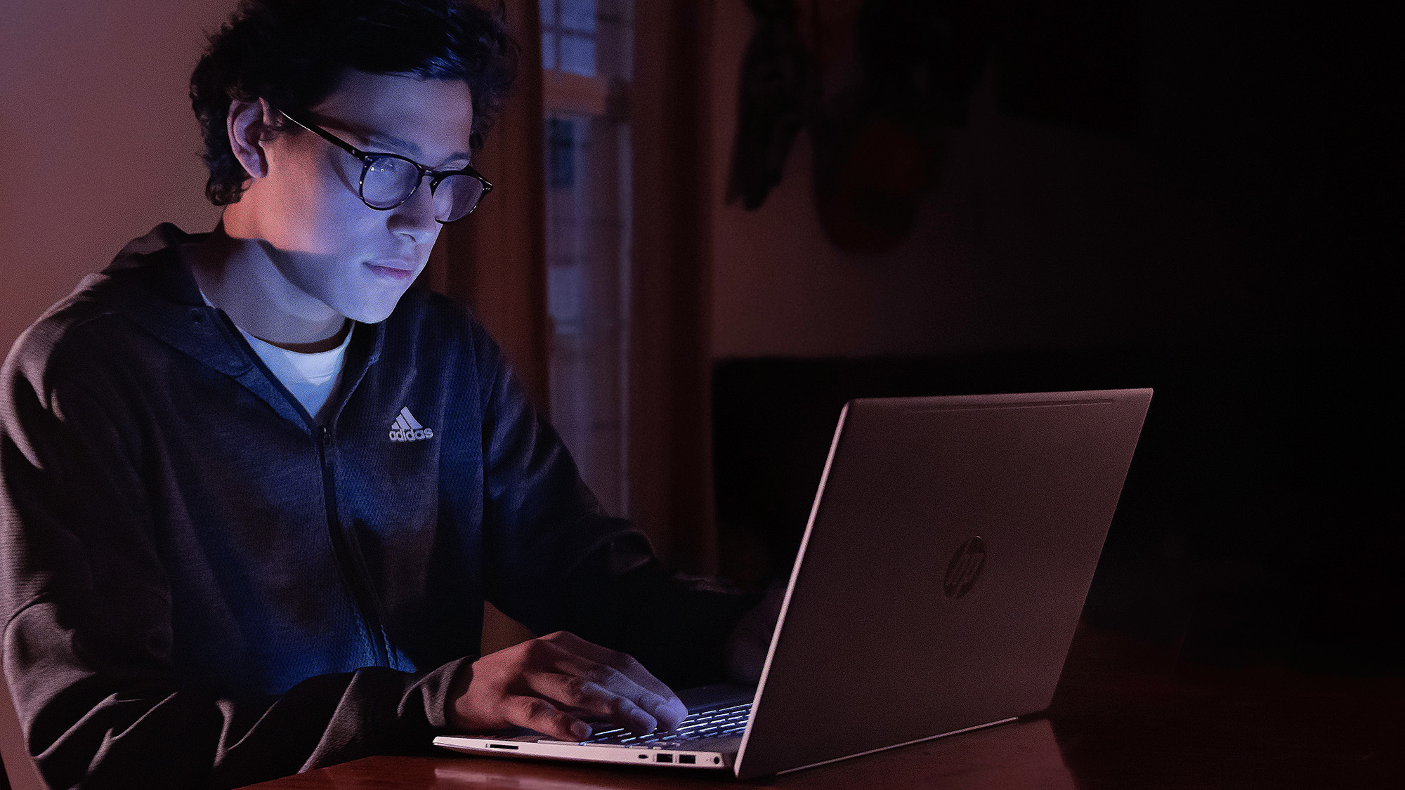 Person with glasses working on computer in the dark, probably trying to find dark patterns on websites.