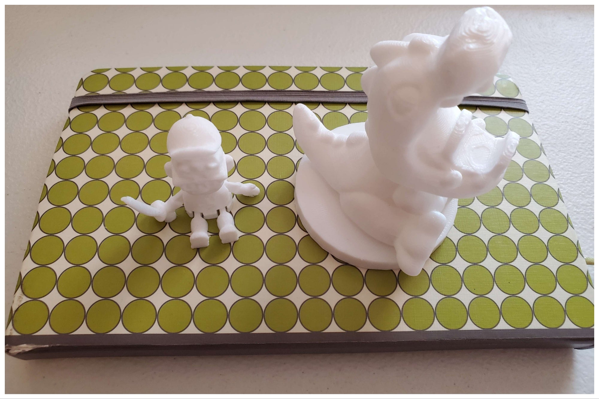 Two coconut white Toybox 3D printer figures on a green notebook
