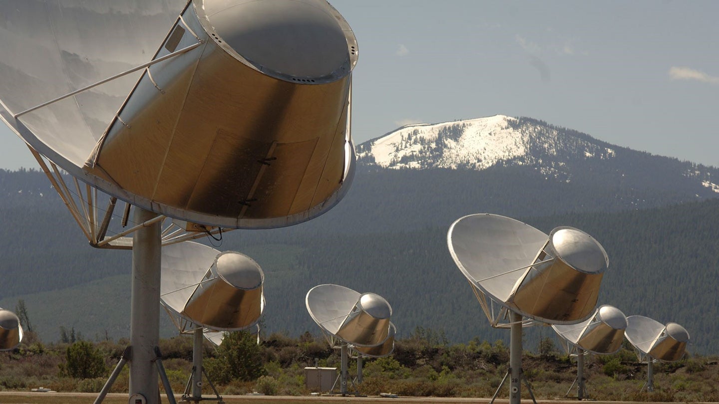 Silver radio telescopes with mountains in the background.