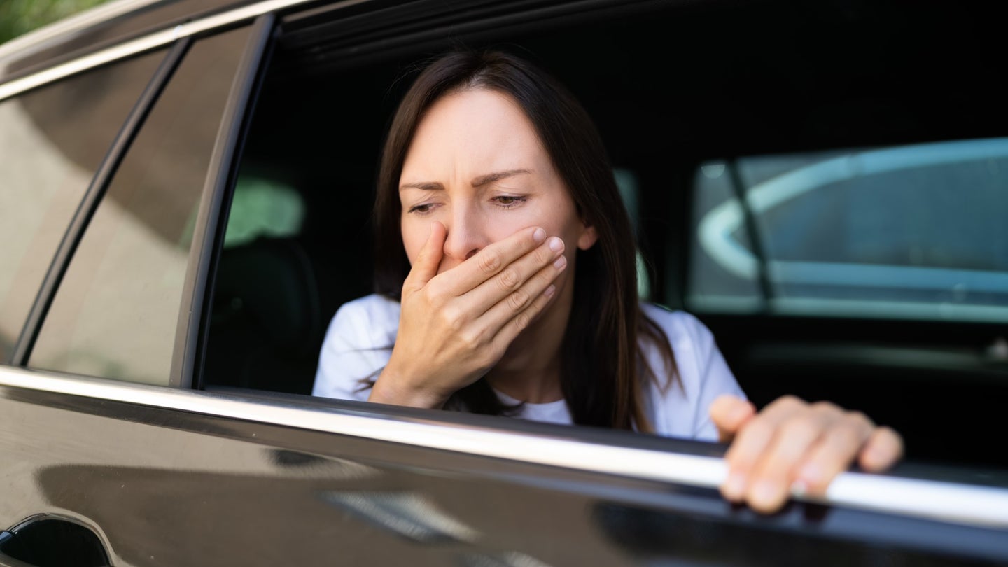 A car passenger appears to feel nauseous with her hand to her mouth.