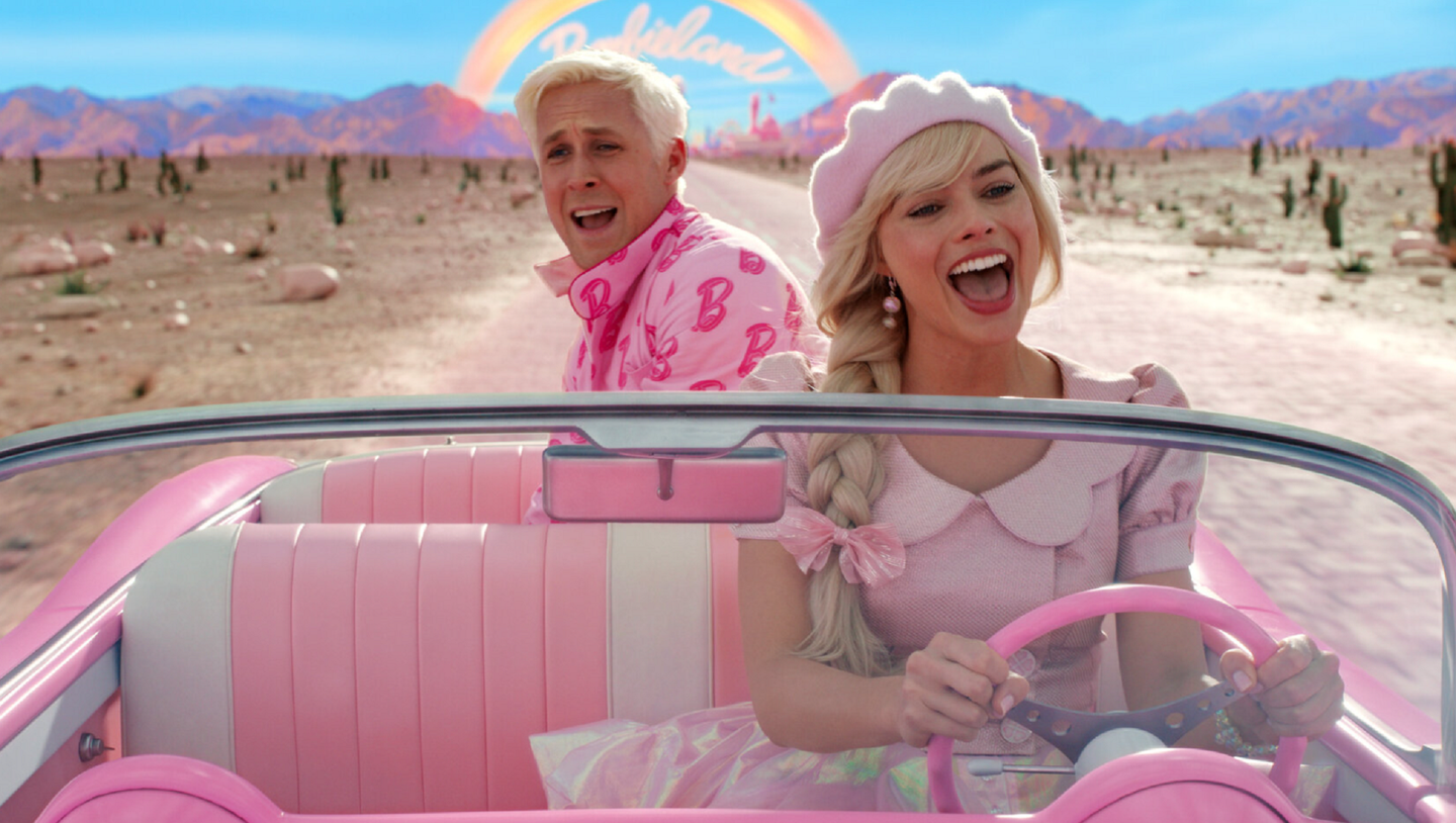 Barbie and Ken in all-pink outfits driving in a pink convertible in the new movie "Barbie"