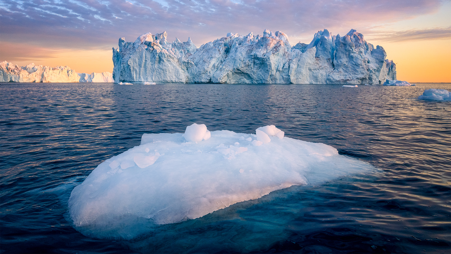 The sun sets over a large ice berg in Greenland, with a large chunk of fallen ice floating in the ocean. Greenland’s continental glacier covers about 80 percent of the 836,3000-square-mile land mass.