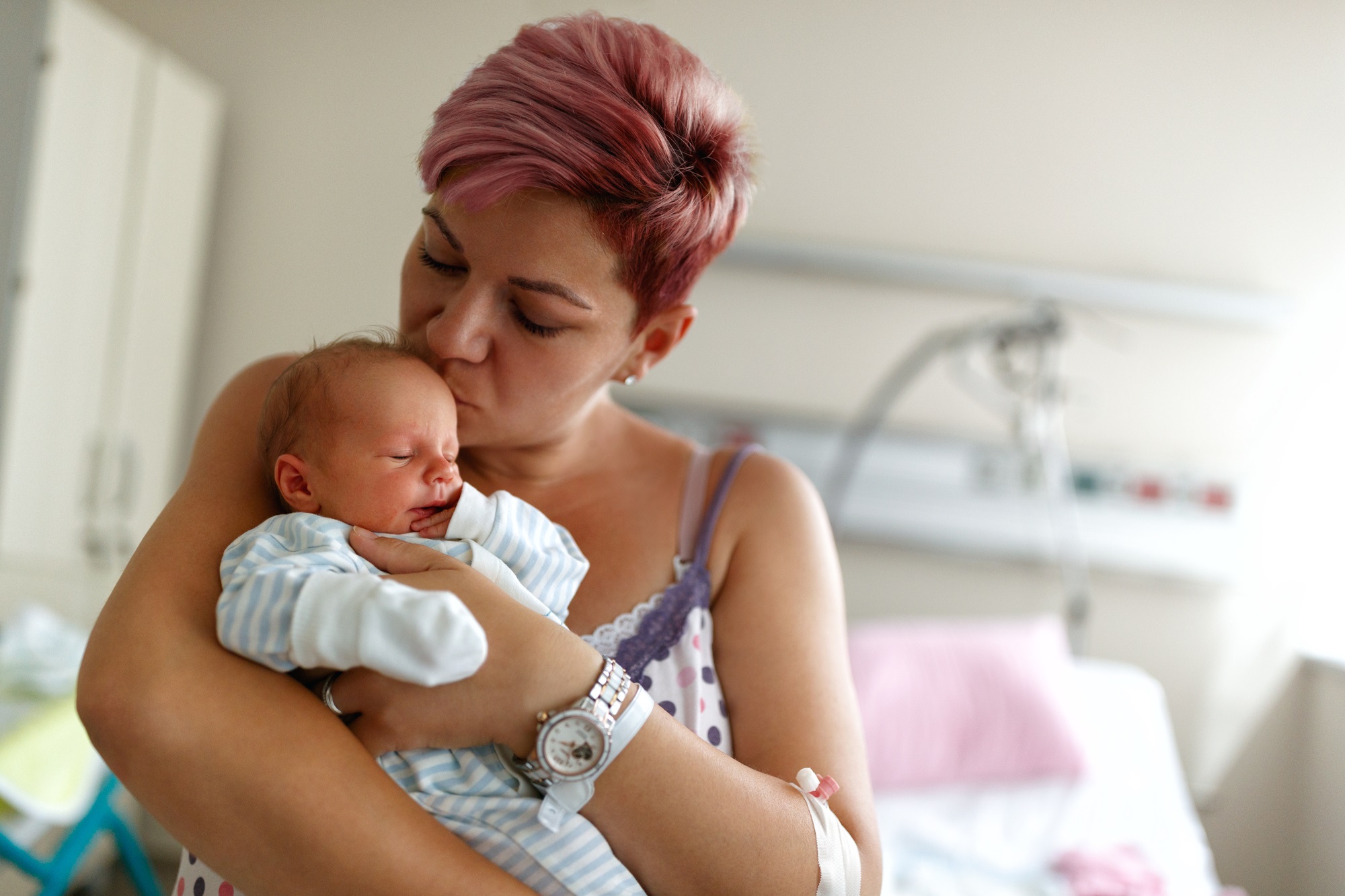 Mother with short pink hair kissing newborn in hospital after induced labor at 39 weeks