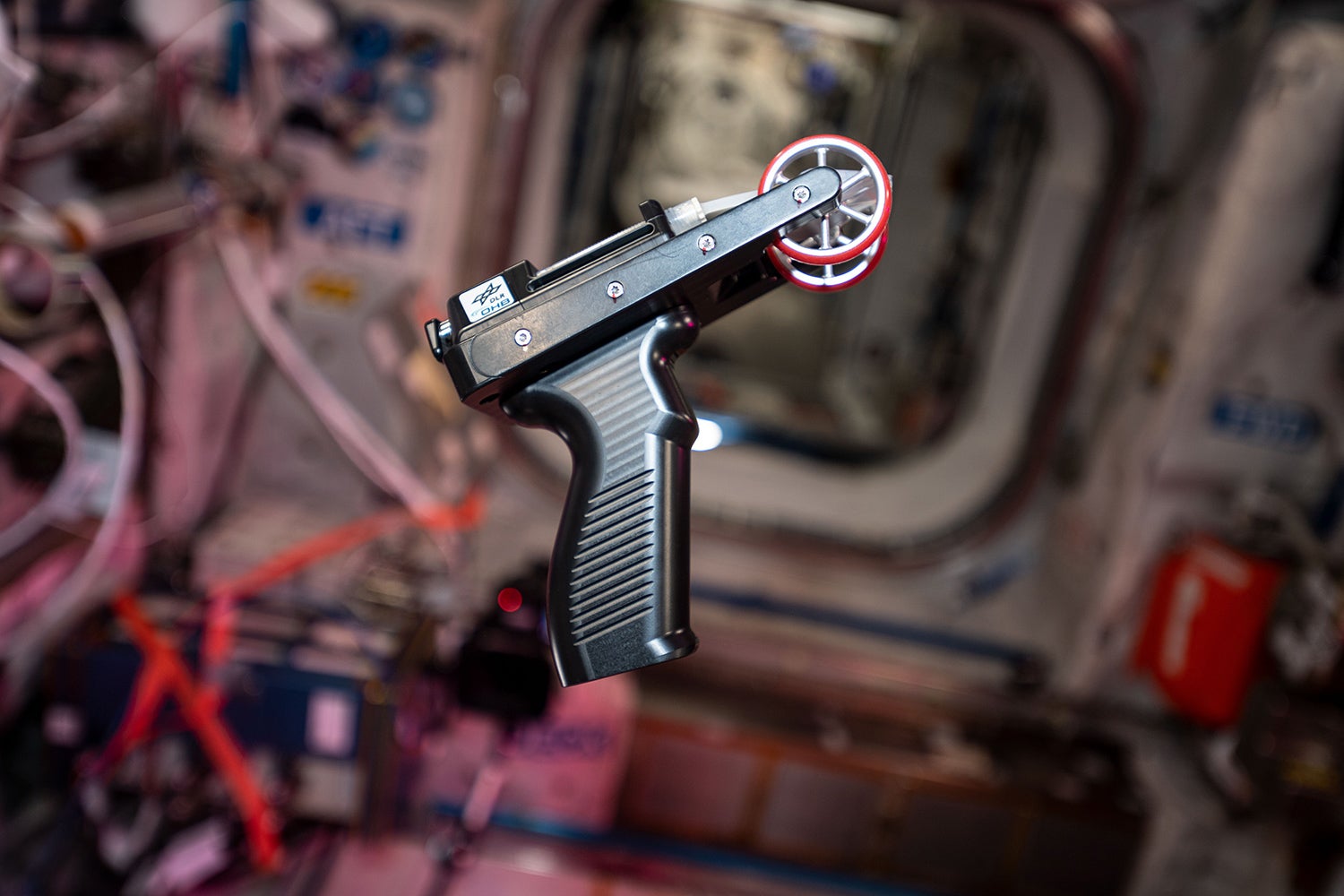 small gunlike tool with red wheels floats in zero gravity